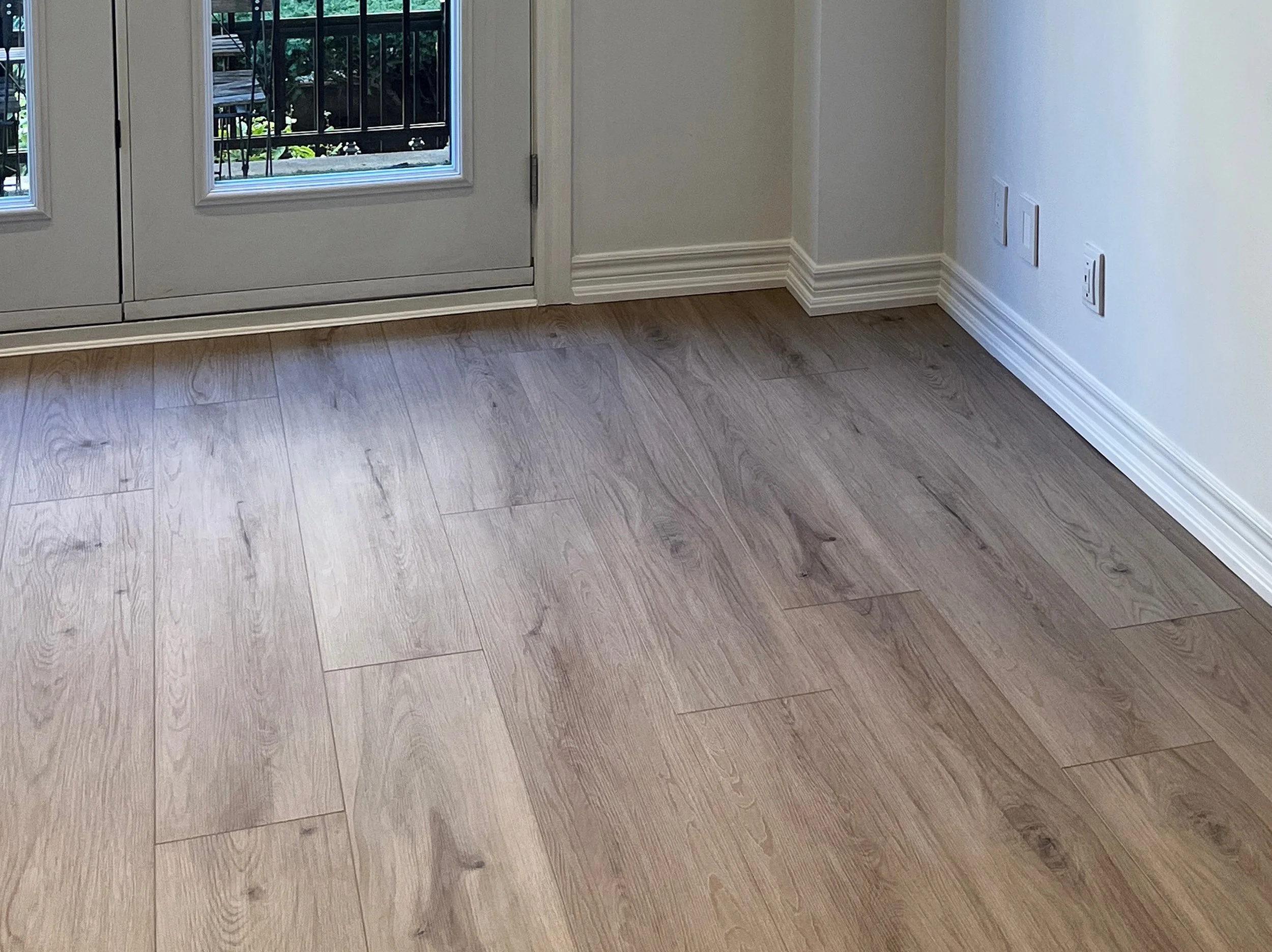 New luxury vinyl flooring installed in a room with white French doors leading to a wrought-iron balcony