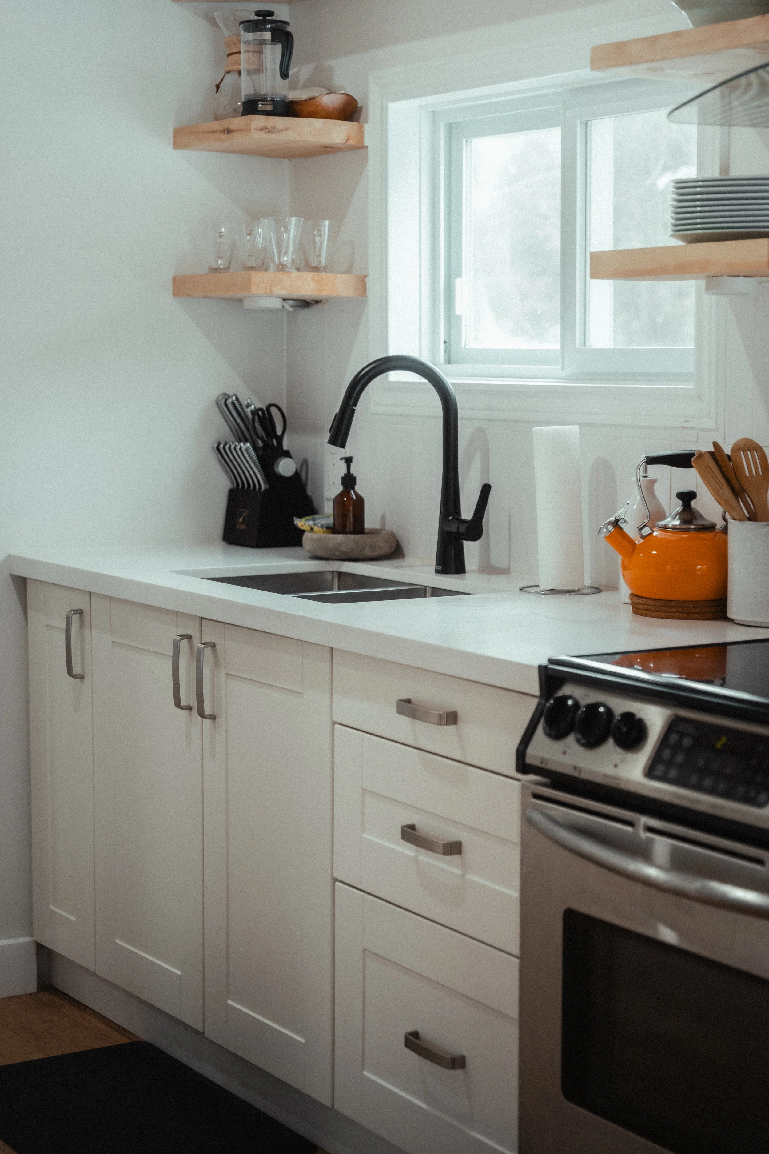 Renovated kitchen with white shaker cabinets, a matte black pull-down faucet, floating wood shelves, and a stainless steel range