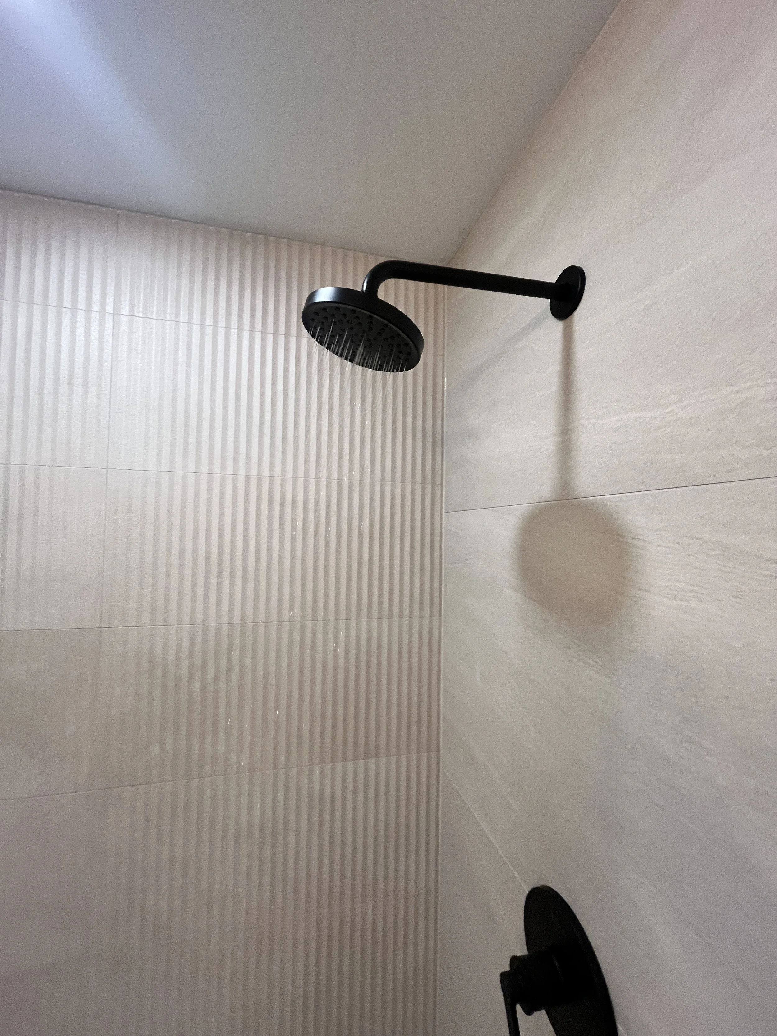 Matte black rain showerhead running against fluted tile in a Queen West condo bathroom renovation