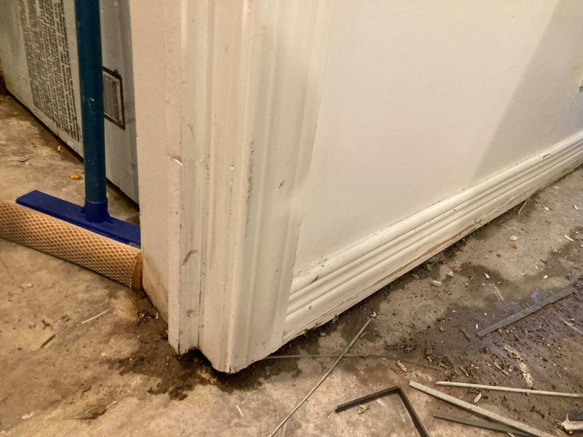 Close-up of existing white baseboard trim and subfloor during demo, with evidence of water coming in from outside
