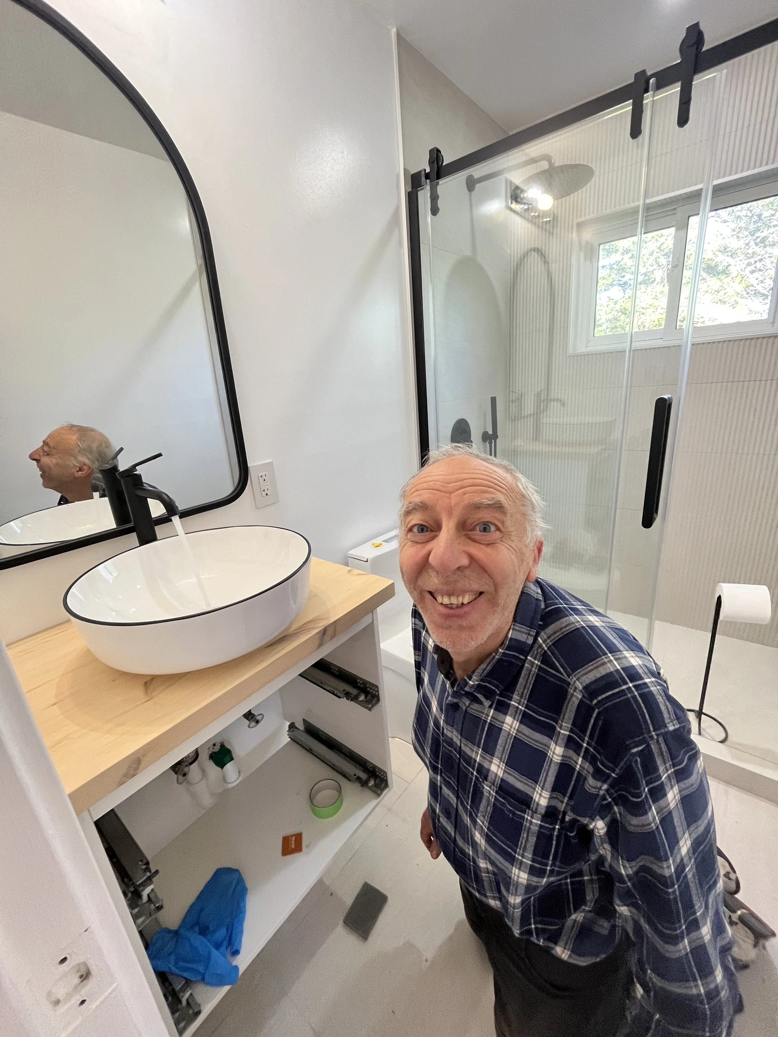 Yuriy smiling next to a finished vessel sink vanity and glass shower enclosure in a completed bathroom renovation