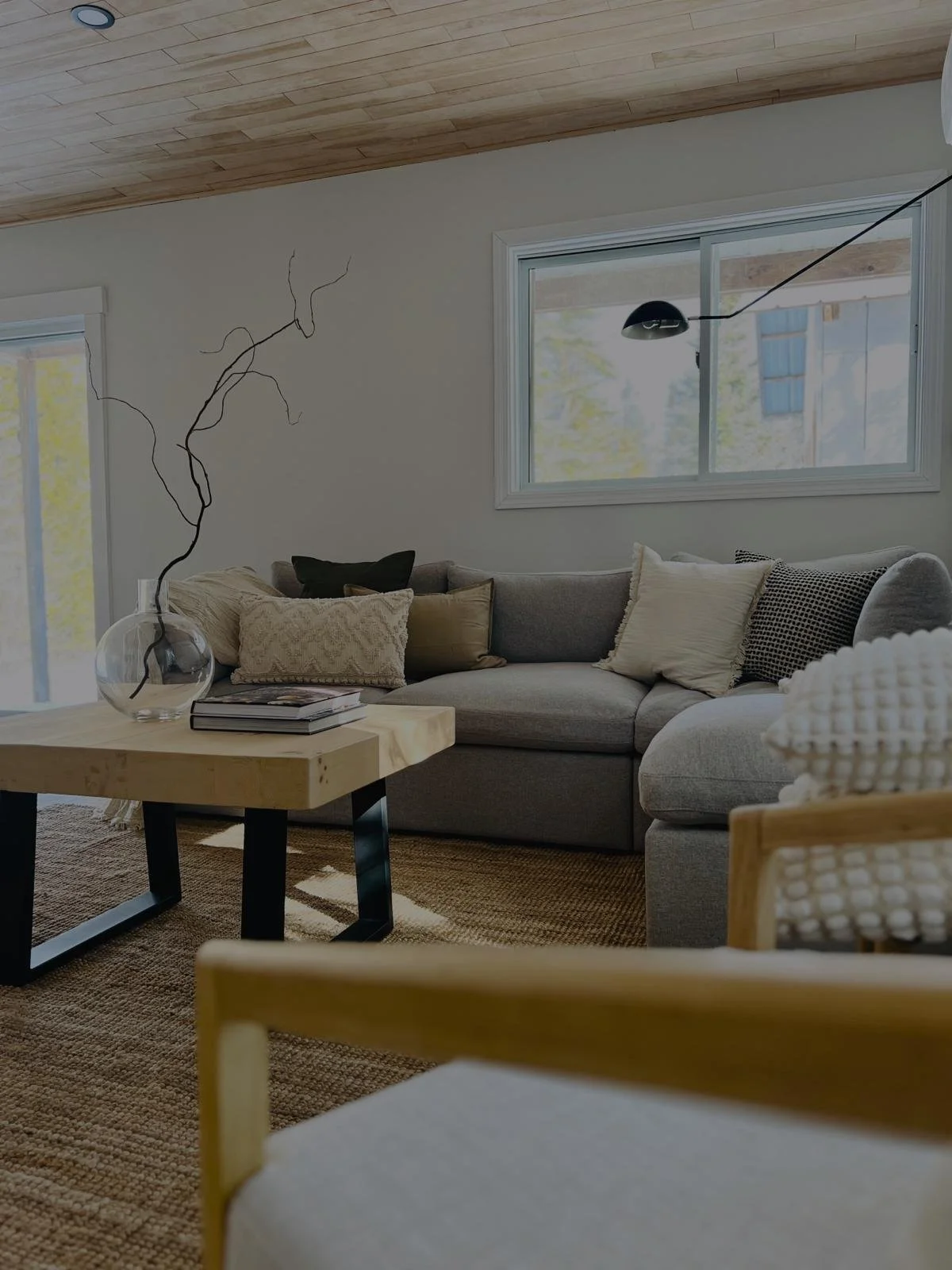 Renovated living room in Toronto with a light wood plank ceiling, grey sectional sofa, wooden coffee table, and woven jute rug