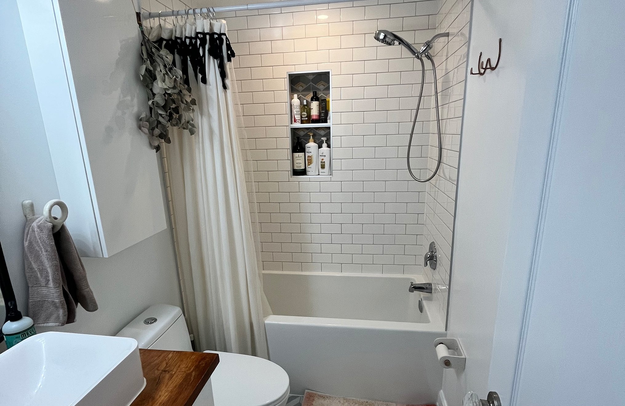 After photo of THE OASIS bathroom renovation with white subway-tiled tub and shower, a recessed tile niche for toiletries, and matte black hardware