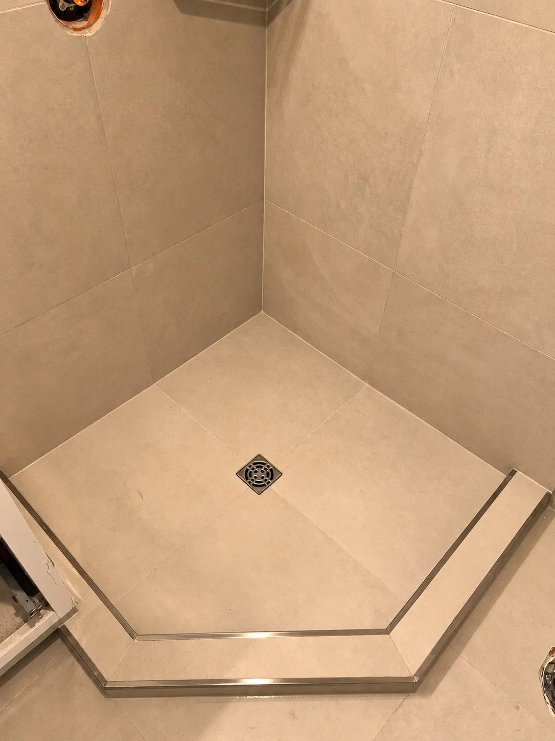 Freshly tiled corner shower pan with a square drain and metal threshold trim, during The Rebuild bathroom renovation
