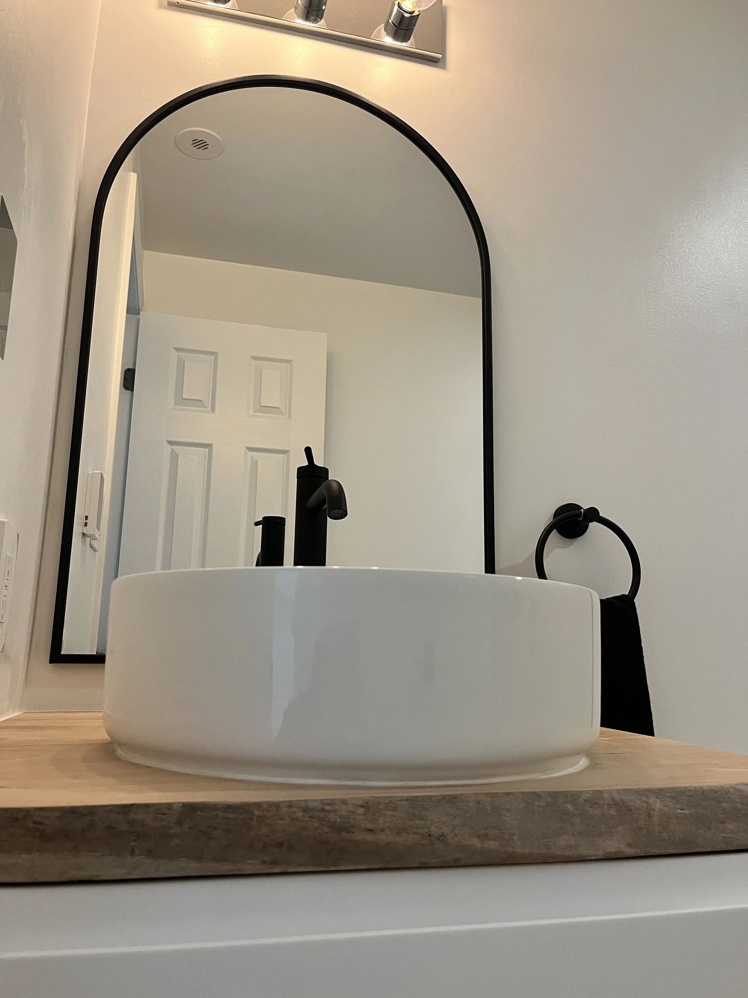 Close-up of a round vessel sink, matte black faucet, and arched black-framed mirror in a Queen West condo bathroom renovation