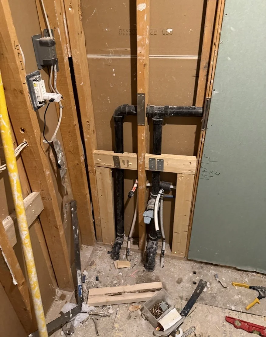 Exposed wall framing with new black ABS drain pipes and supply lines being rerouted during The Rebuild bathroom renovation