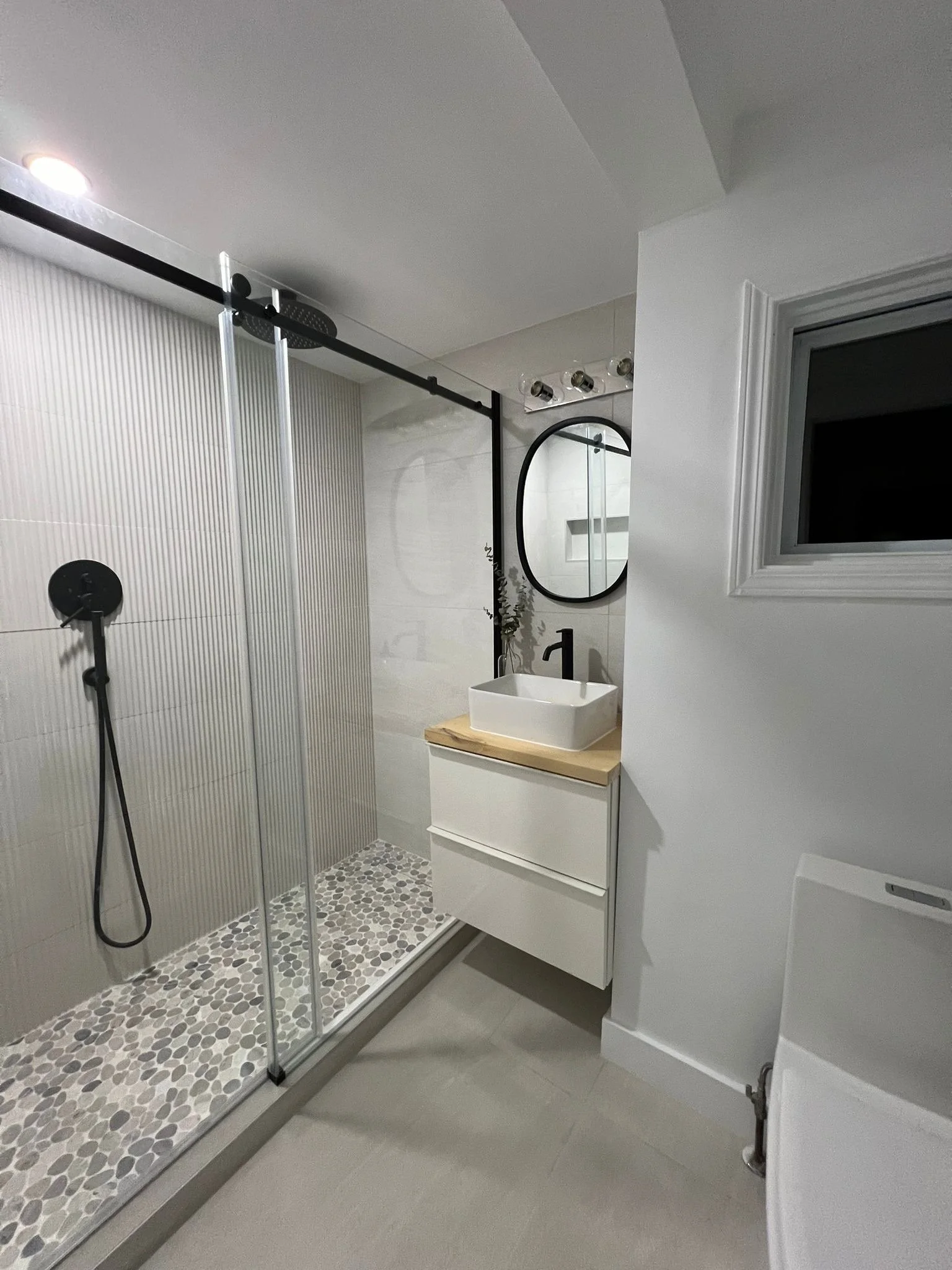 Bathroom in the Tobermory cottage renovation with a fluted tile walk-in shower, matte black fixtures, a round vessel sink, and a black-framed round mirror