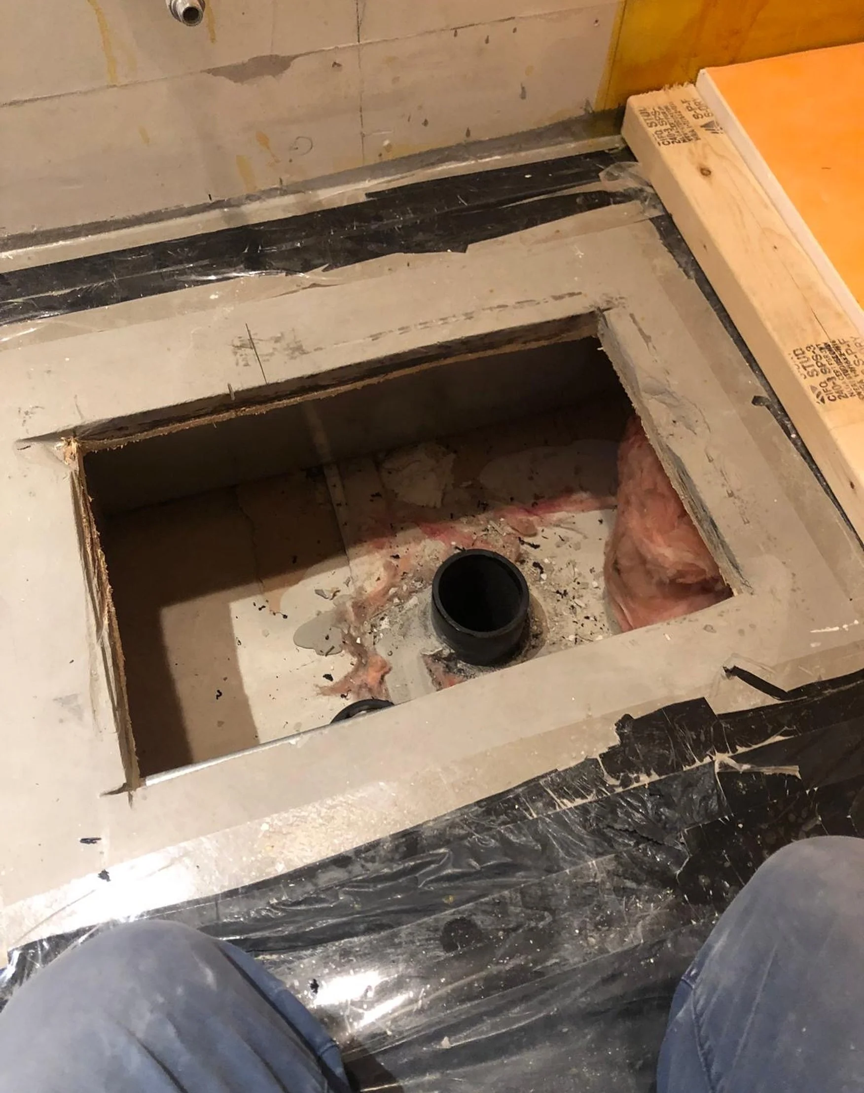 Opened floor section showing a drain pipe, insulation, and vapour barrier during rough plumbing work in the Queen West condo bathroom renovation