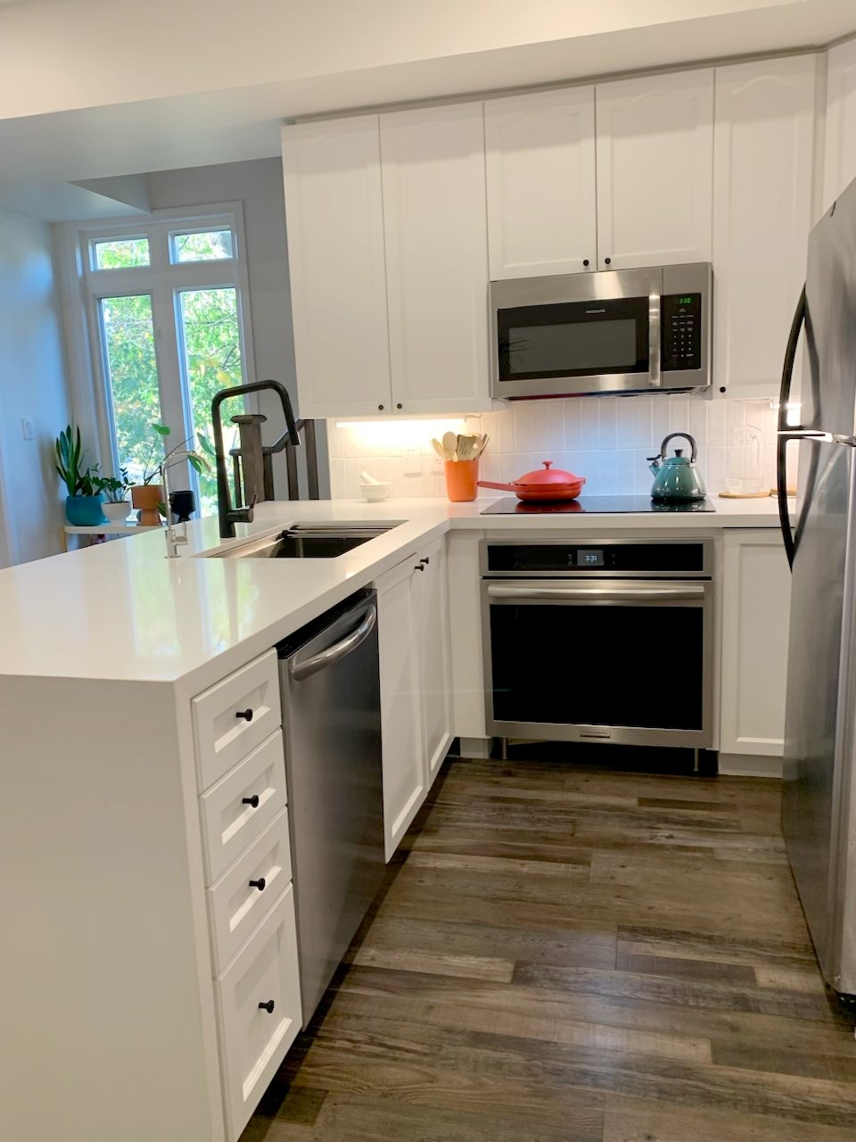 Full view of THE OASIS kitchen renovation with white shaker cabinets, stainless steel appliances, a white L-shaped island, and wood-look flooring