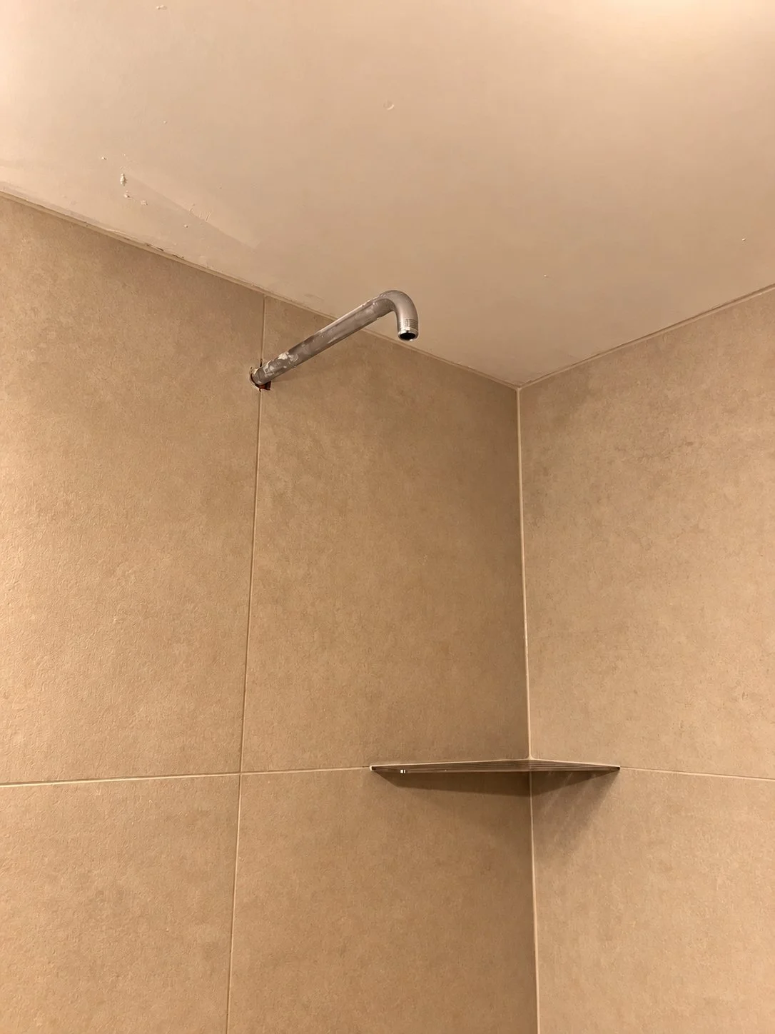 Shower arm roughed in above a built-in corner shelf, with ceiling patching still visible, during The Rebuild bathroom renovation