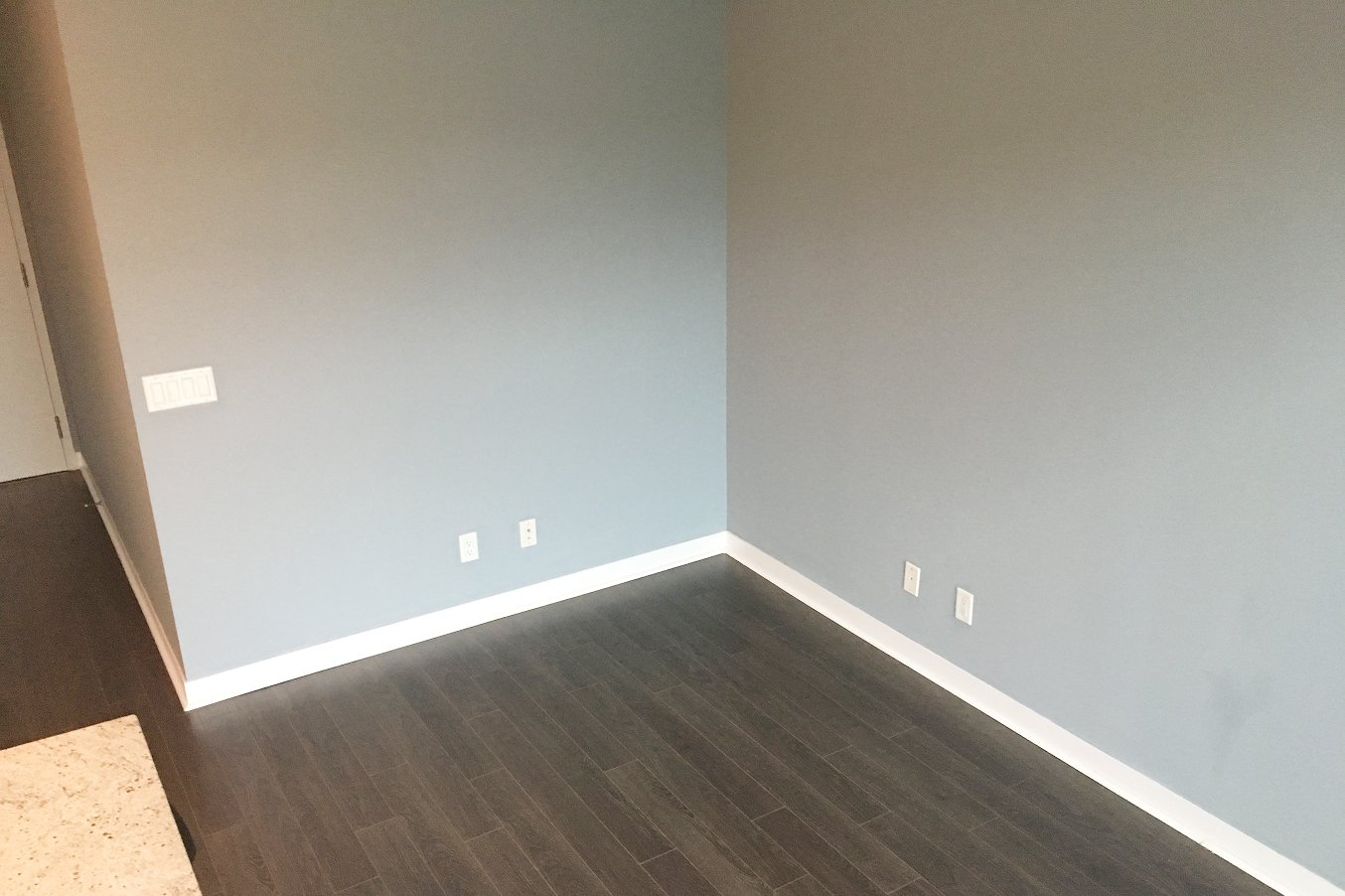 Before photo of an empty room with blue walls and dark wood-look flooring in the iLOFT Etobicoke renovation, ahead of the full transformation