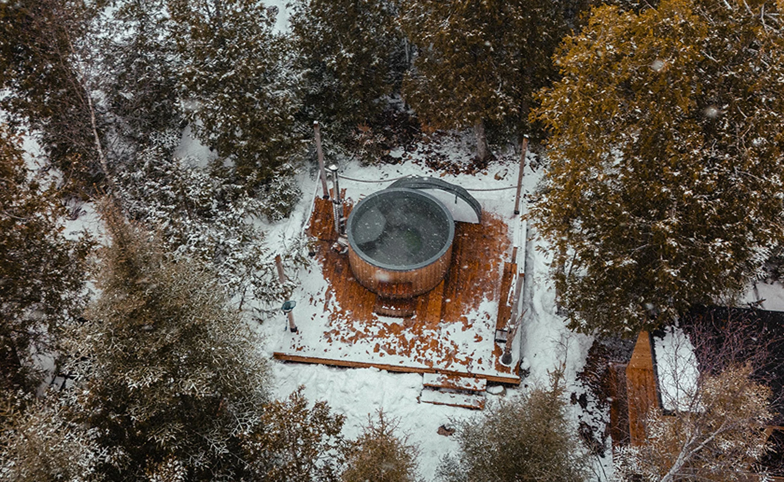 Aerial view of a wood-fired hot tub on a private outdoor deck, tucked into a snow-dusted forest at the Tobermory cottage renovation