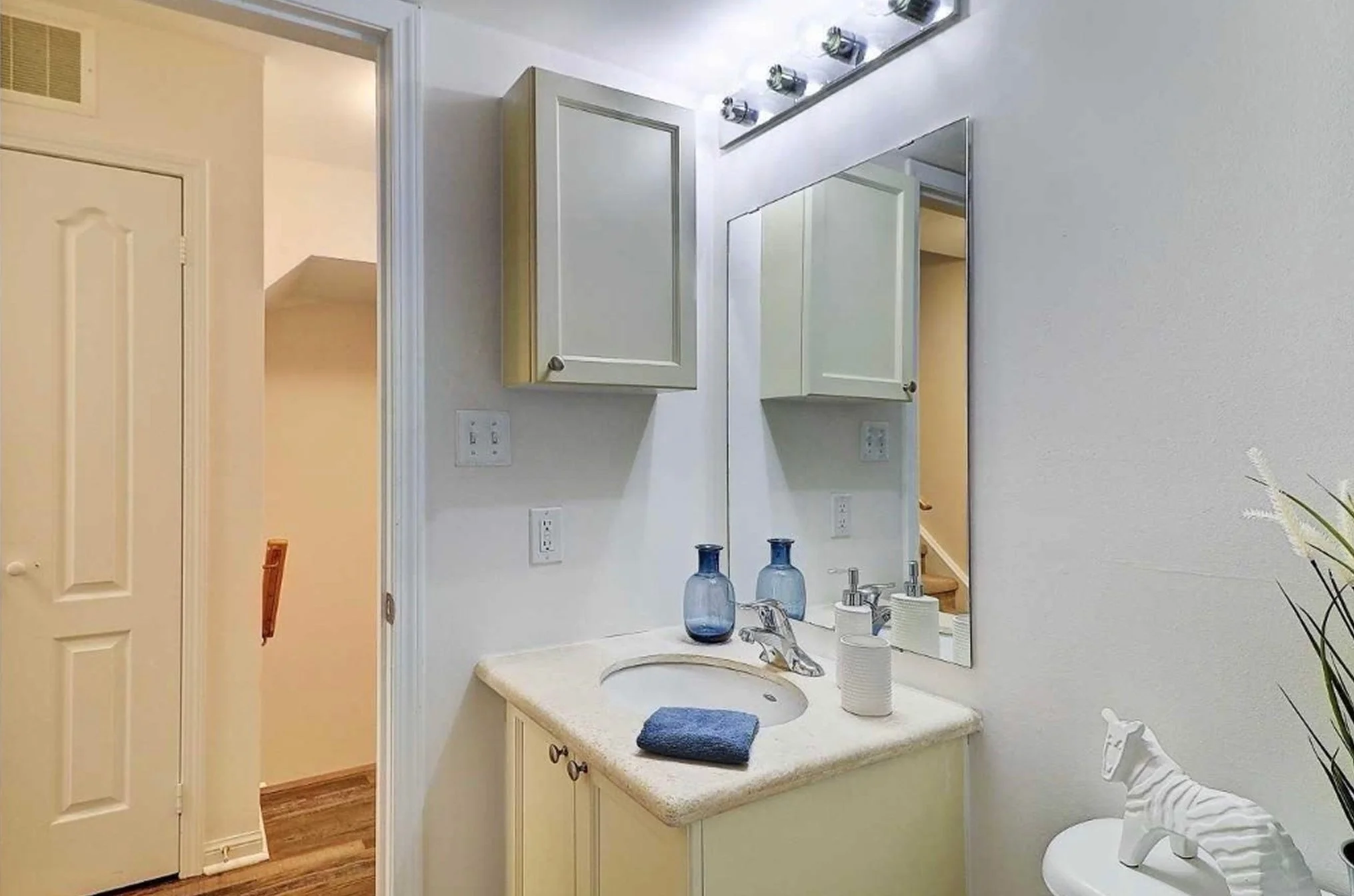 Before photo of THE OASIS bathroom with a dated cream vanity, chrome light fixture, and medicine cabinet, ahead of the full renovation