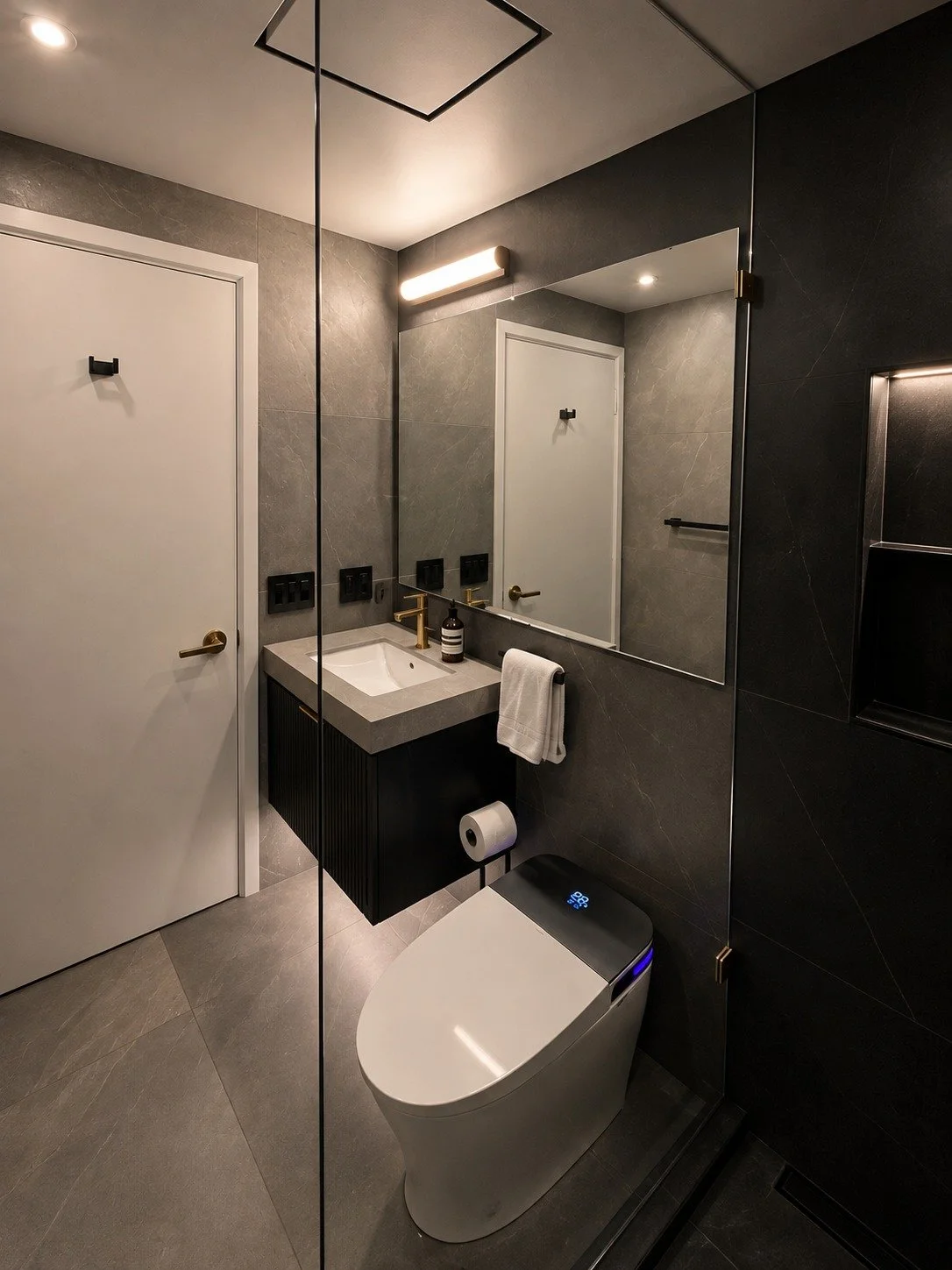 LUX NOIR bathroom with charcoal stone-look tile, floating black fluted vanity, brushed gold faucet, smart toilet and frameless glass shower.