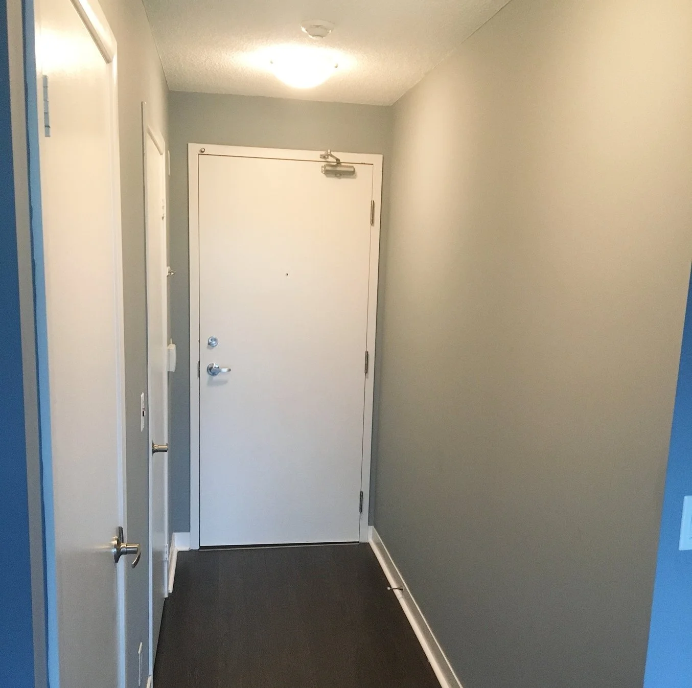 Before photo of the iLOFT entryway with grey walls, a white front door, and dark wood flooring, ahead of the full renovation