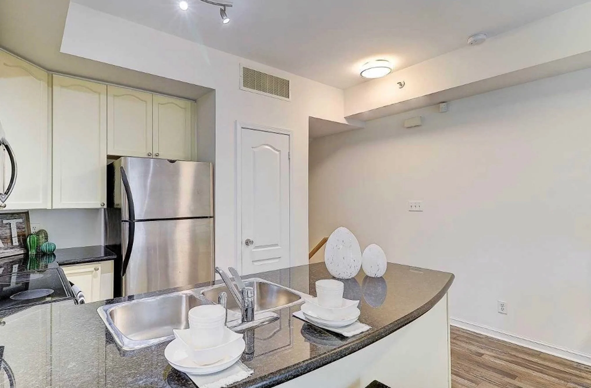 Before photo of THE OASIS kitchen with dated cream cabinets, a black granite countertop, and stainless steel refrigerator, ahead of the full renovation