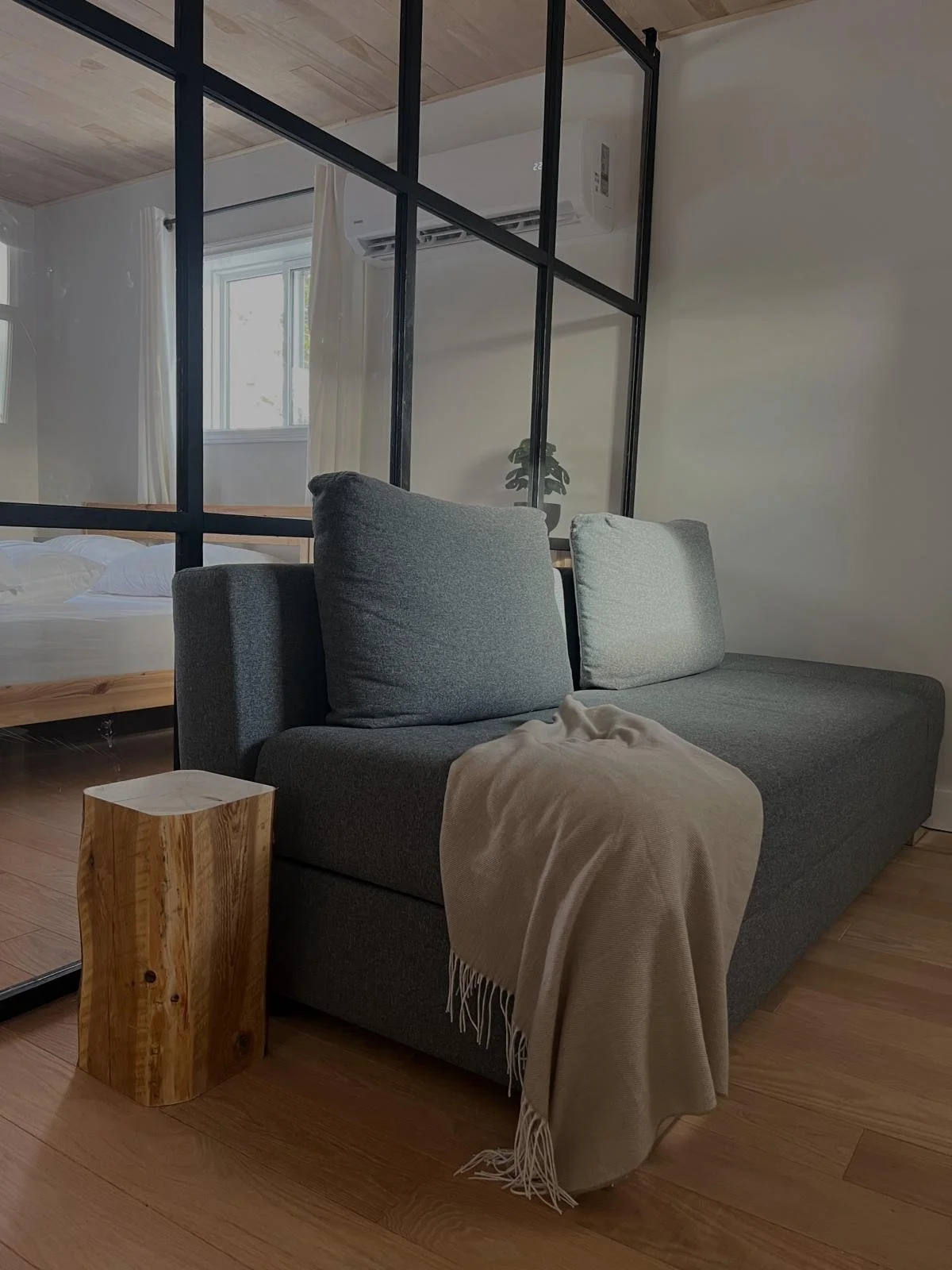 Grey daybed with a draped throw blanket, positioned beside a black-framed glass partition wall opening into the bedroom, in the Tobermory cottage renovation