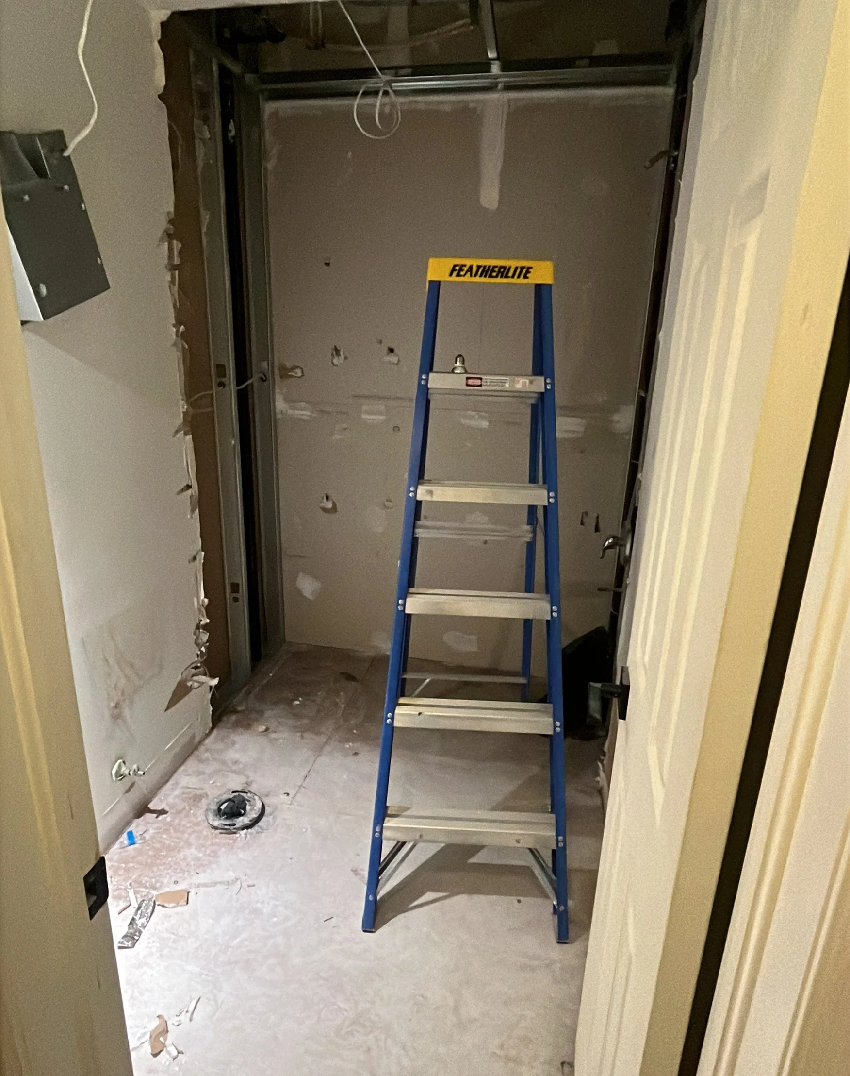 Gutted bathroom stripped down to subfloor and new drywall, with the toilet flange exposed and a step ladder set up, during the Queen West condo bathroom renovation
