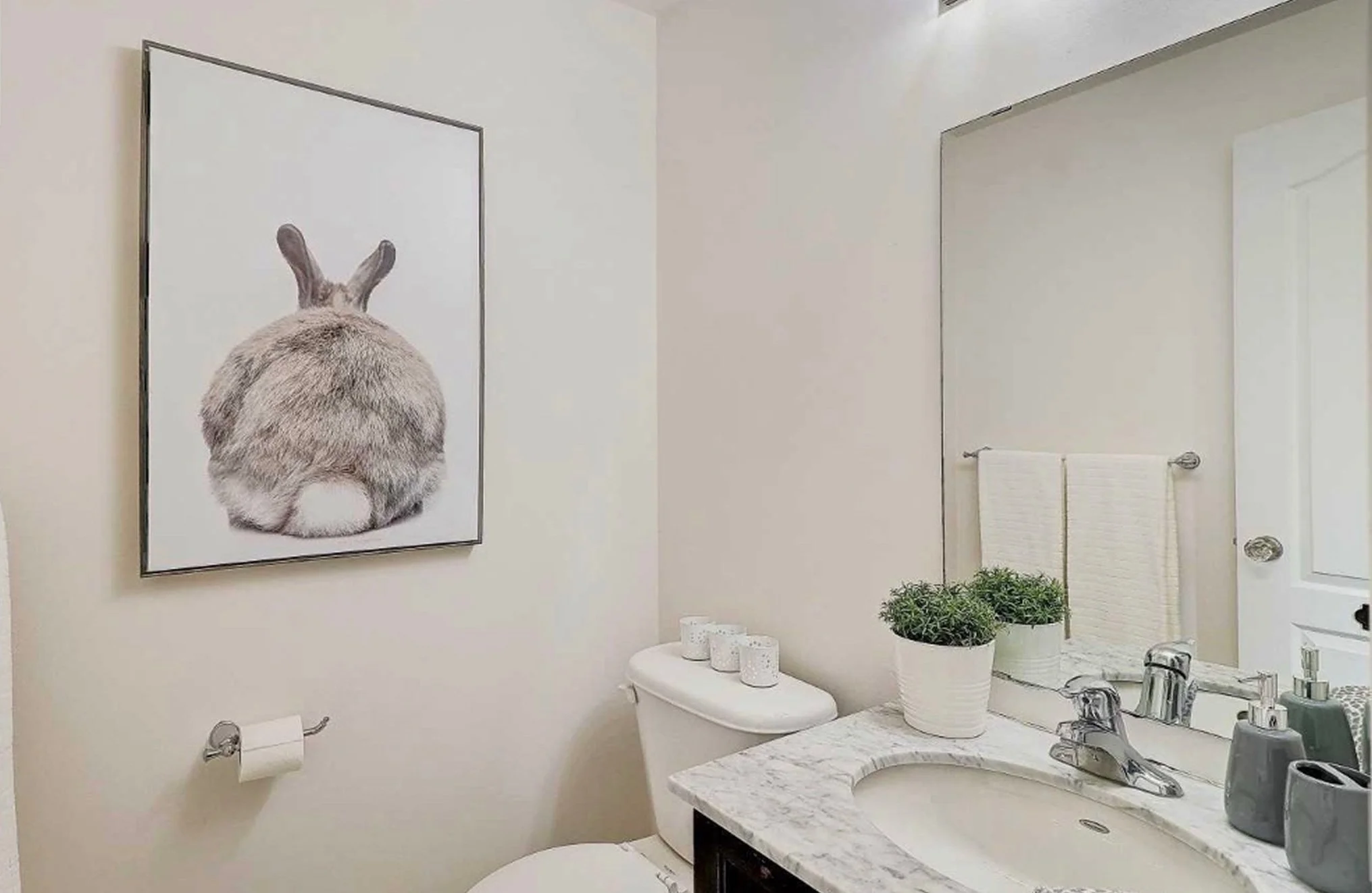 Before photo of THE OASIS powder room, staged with a marble vanity, chrome fixtures, and a framed bunny print, ahead of the full renovation