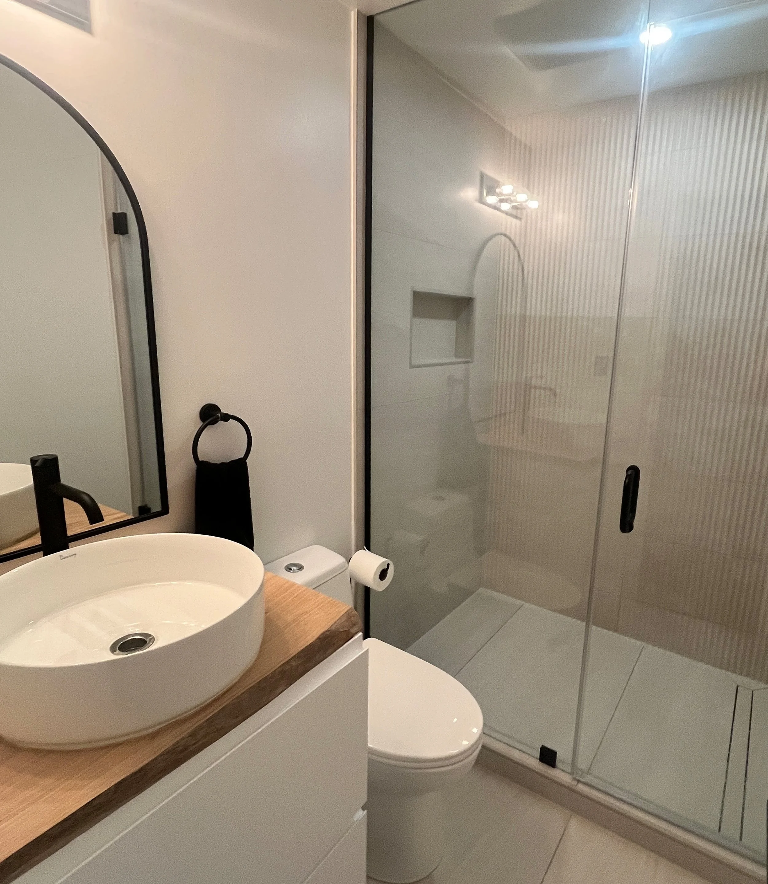 Cropped view of a luxury condo bathroom renovation in Queen West, Toronto, showing the vessel sink vanity, toilet, and frameless glass shower with fluted tile