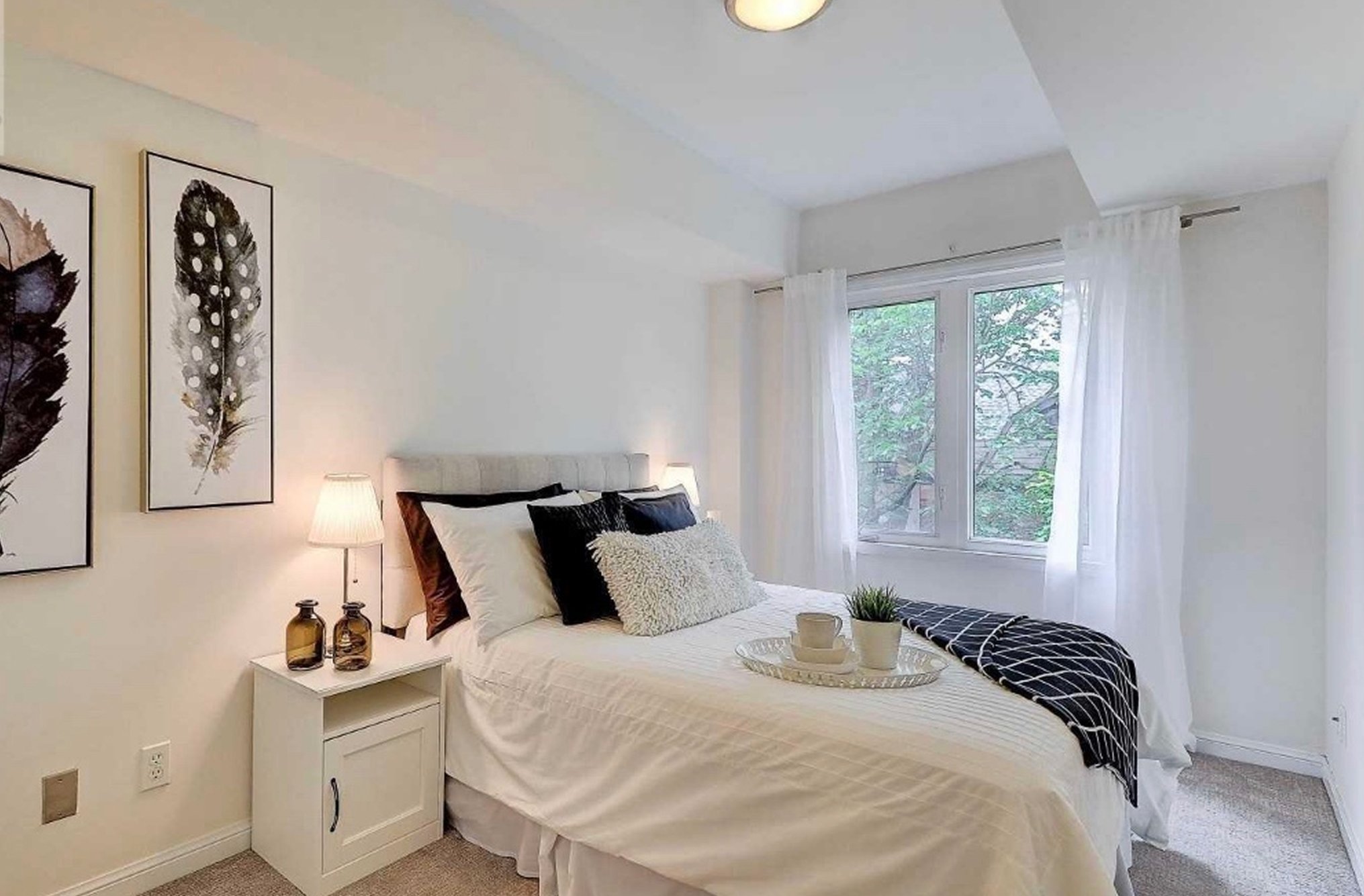 Before photo of THE OASIS bedroom, staged with a beige tufted headboard, feather wall art, and carpet flooring, ahead of the full renovation