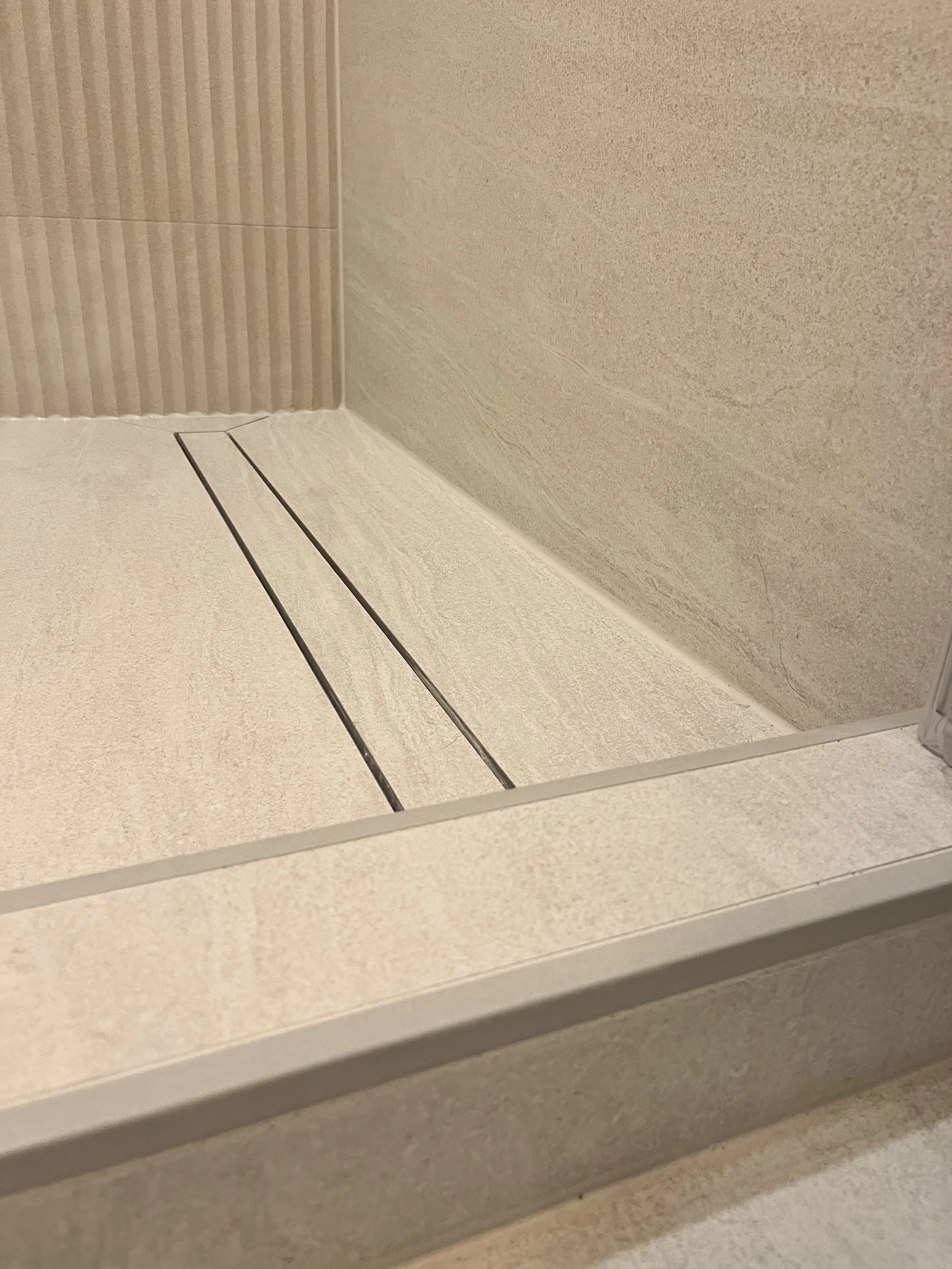 Close-up of a linear shower drain and curbless shower entry in a Queen West condo bathroom renovation, with stone-look tile flooring