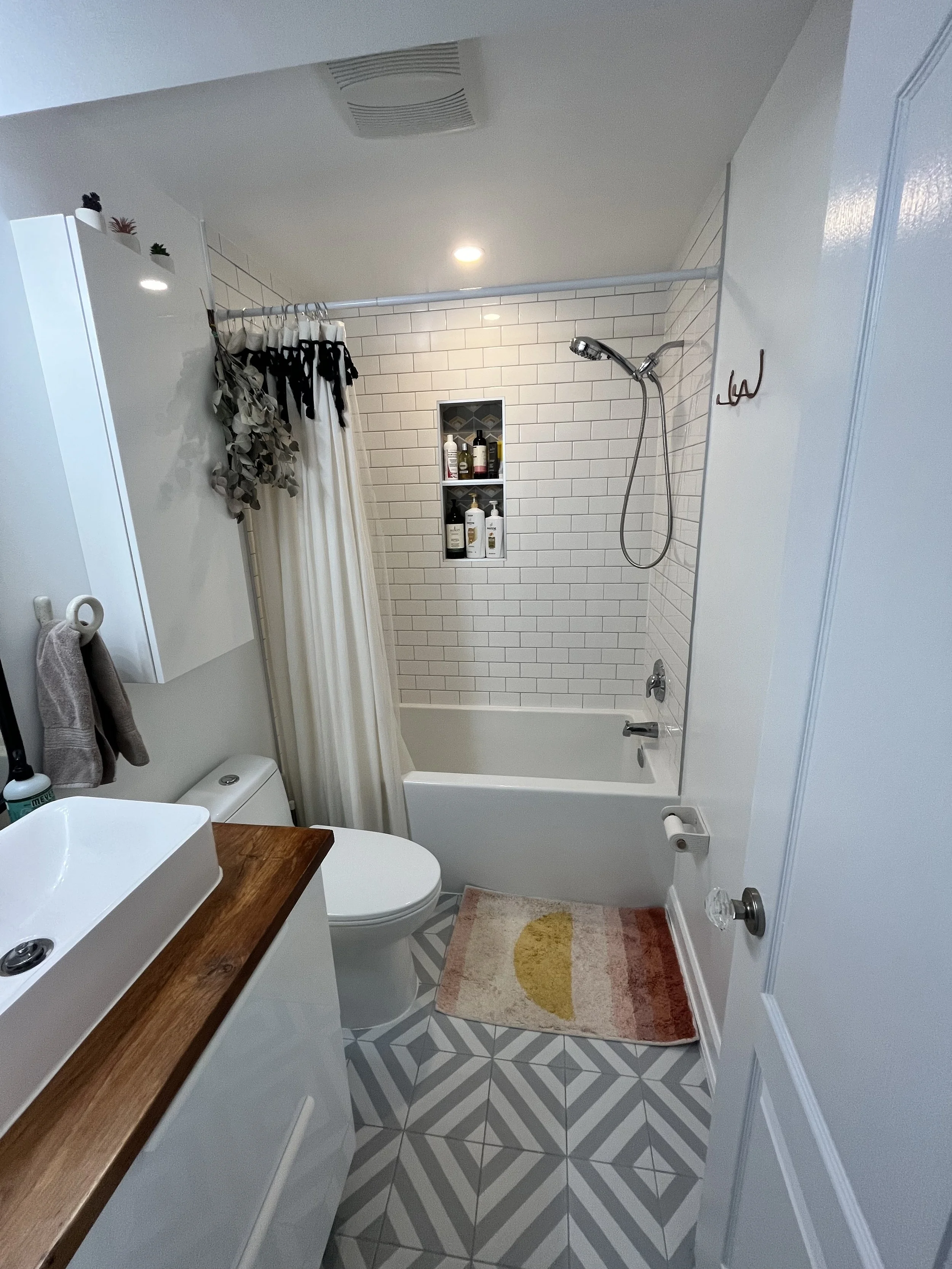 THE OASIS bathroom renovation with a white subway-tiled tub and shower surround, a recessed tile niche for toiletries, and geometric grey and white floor tile