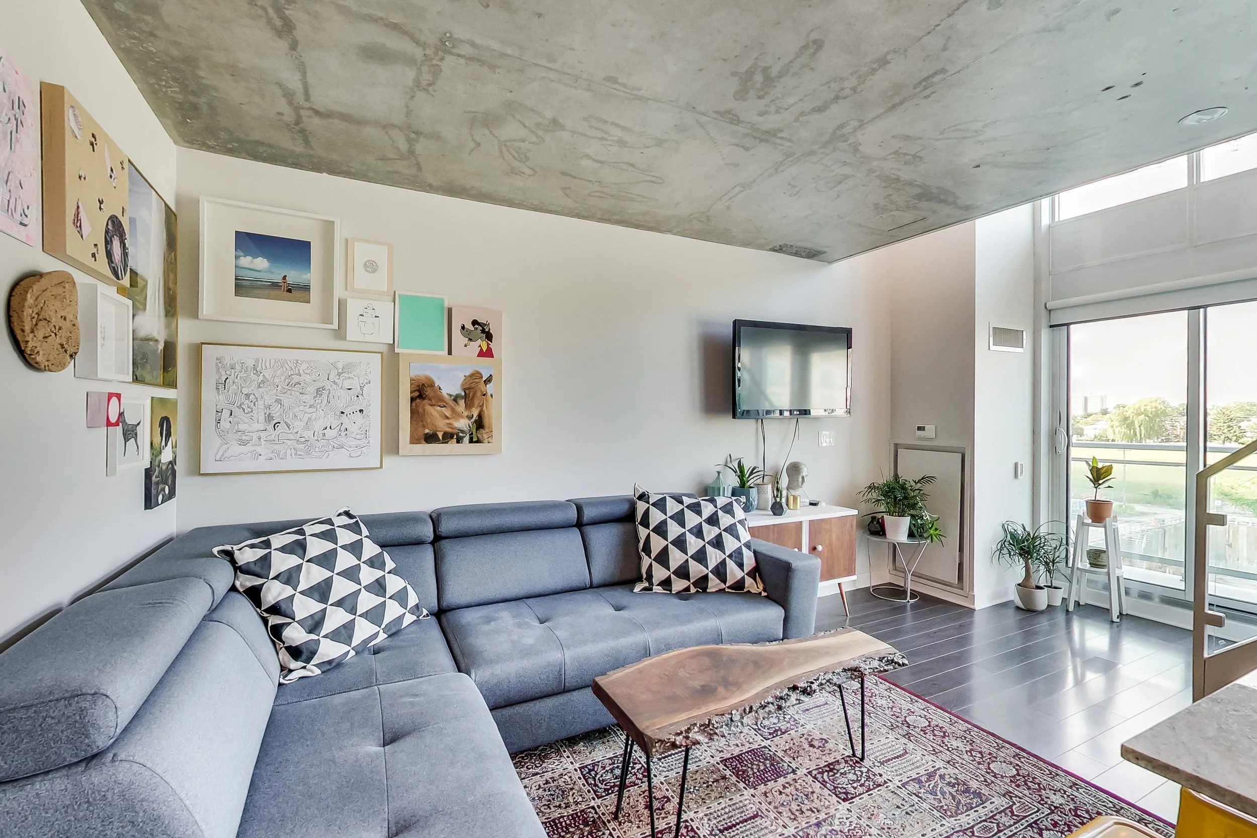 iLOFT living room in Etobicoke with an exposed concrete ceiling, blue sectional sofa, live-edge wood coffee table, and a gallery wall of framed art