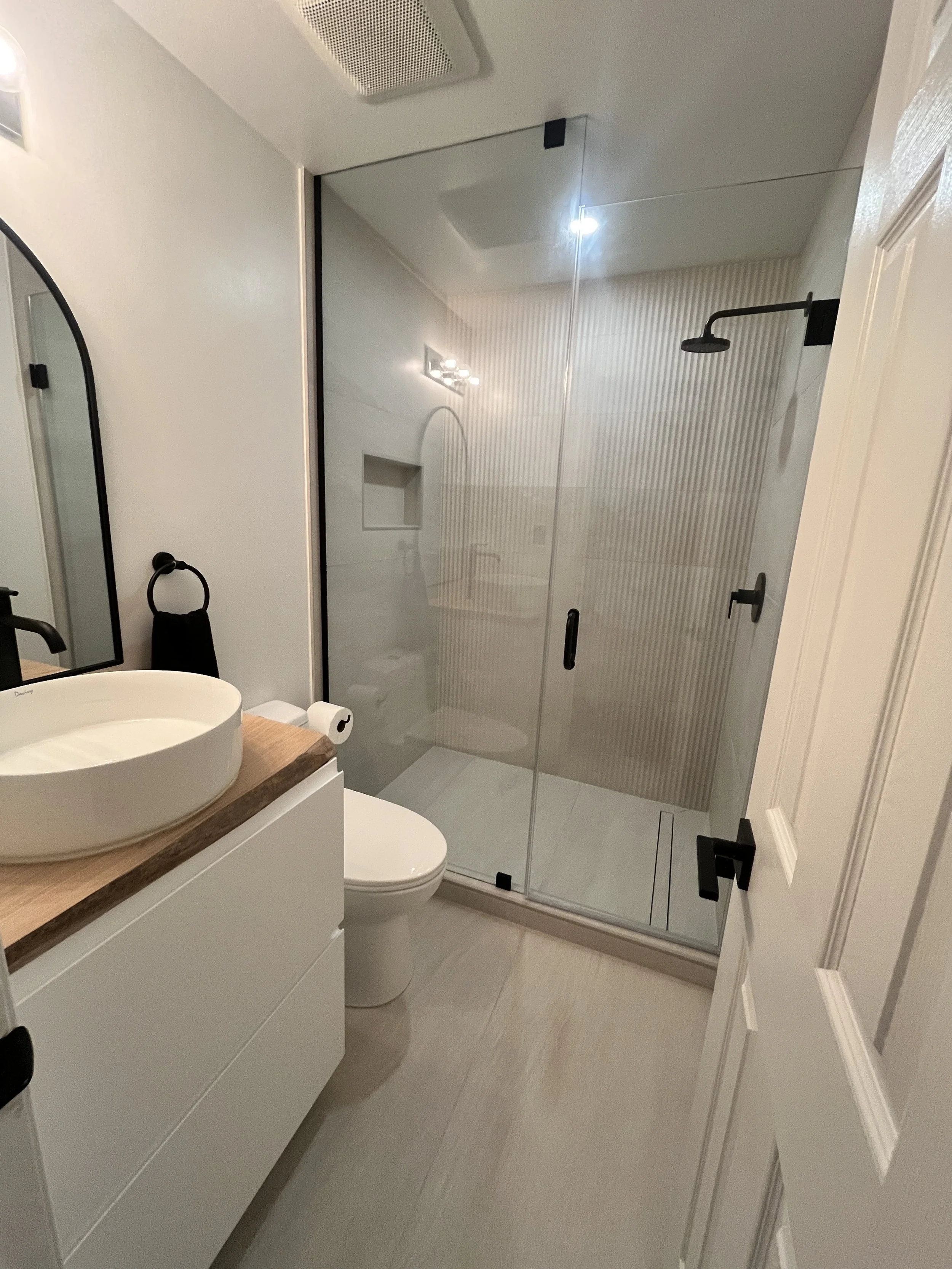 Luxury condo bathroom renovation in Queen West, Toronto with a frameless glass shower, fluted tile, matte black fixtures, and a floating vessel sink vanity