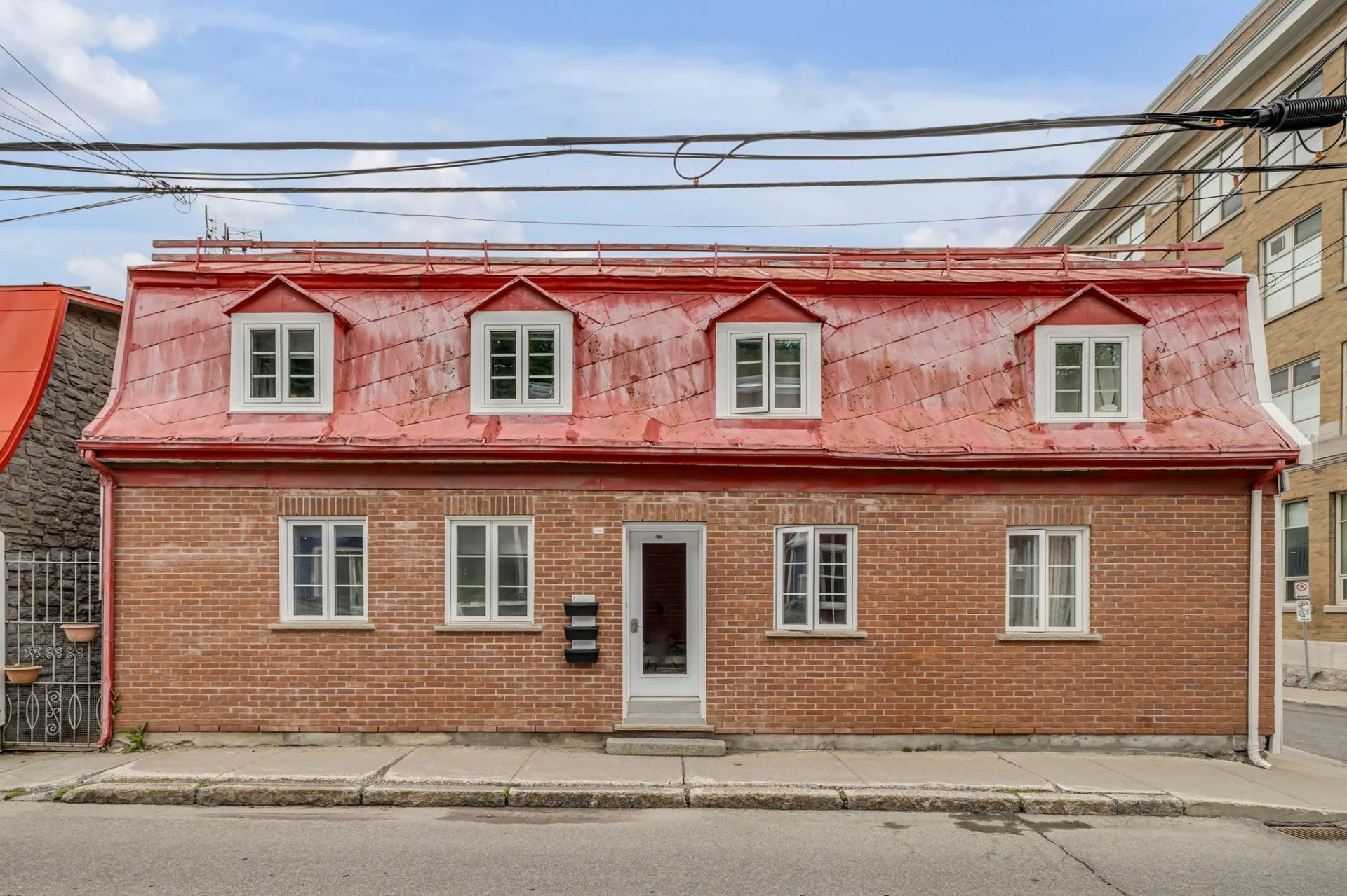 Maison en brique avec un toit en métal rouge et quatre fenêtres en haut, située dans un quartier résidentiel