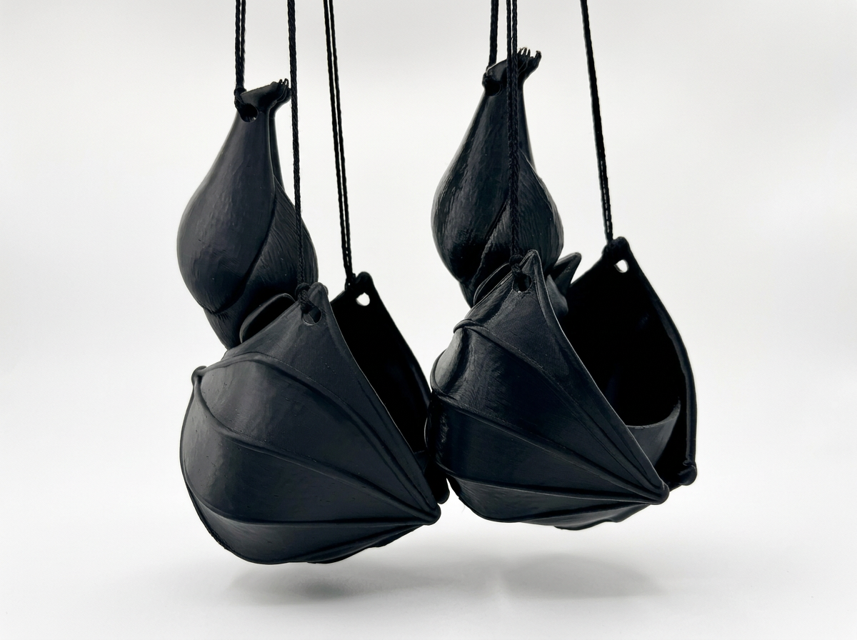 Four black hanging bat planters suspended against a plain off-white studio background
