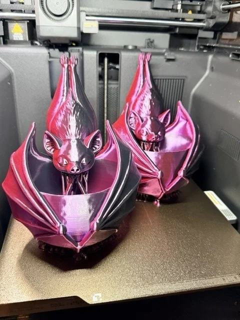 Two pink and black silk bat planters fresh off the 3D printer bed