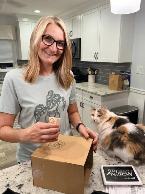Sara sealing a shipping box while her cat Izzy watches from the counter