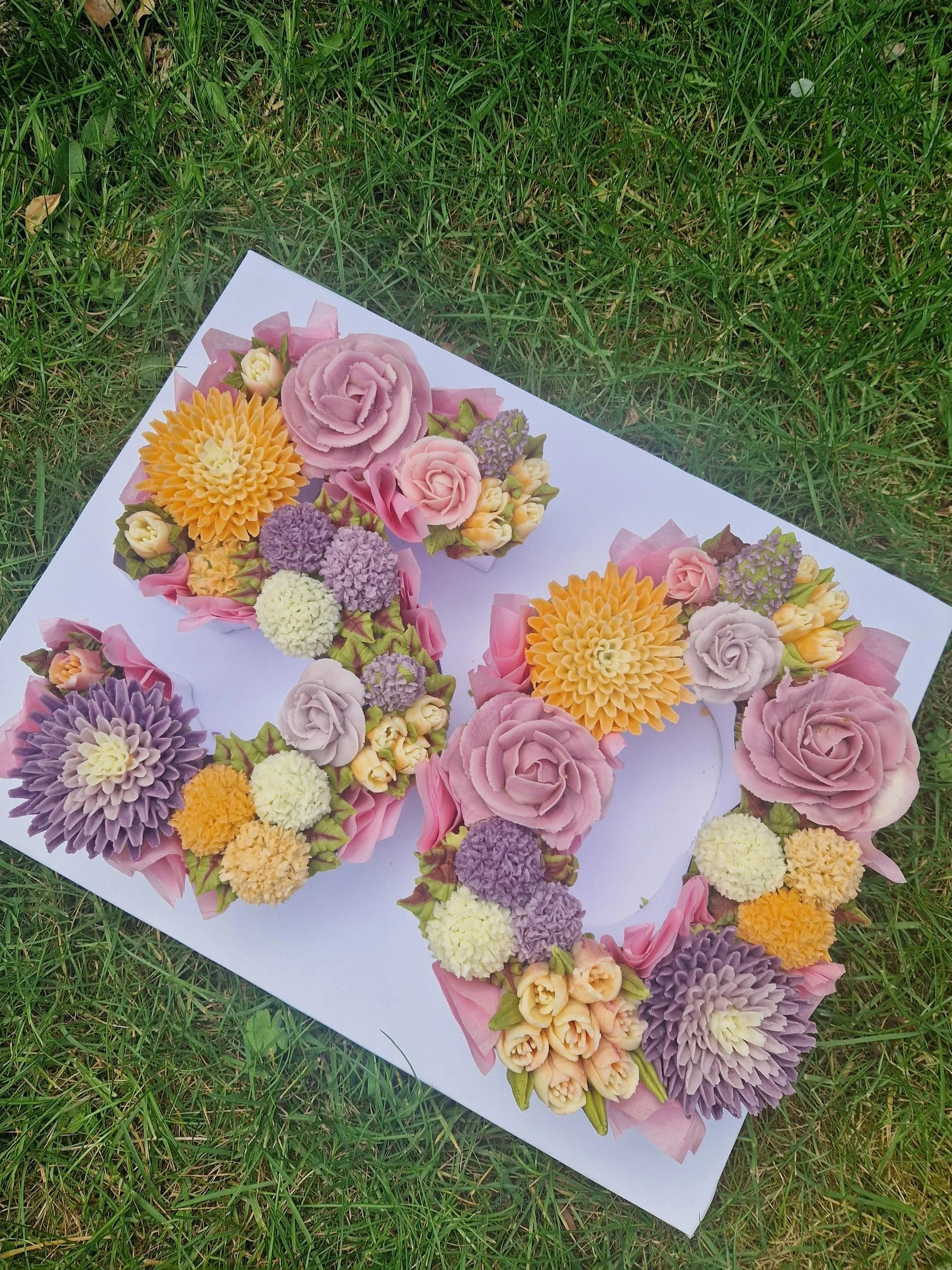 A Cupcake number cake paper with colorful flower-shaped decorations resting on green grass.
