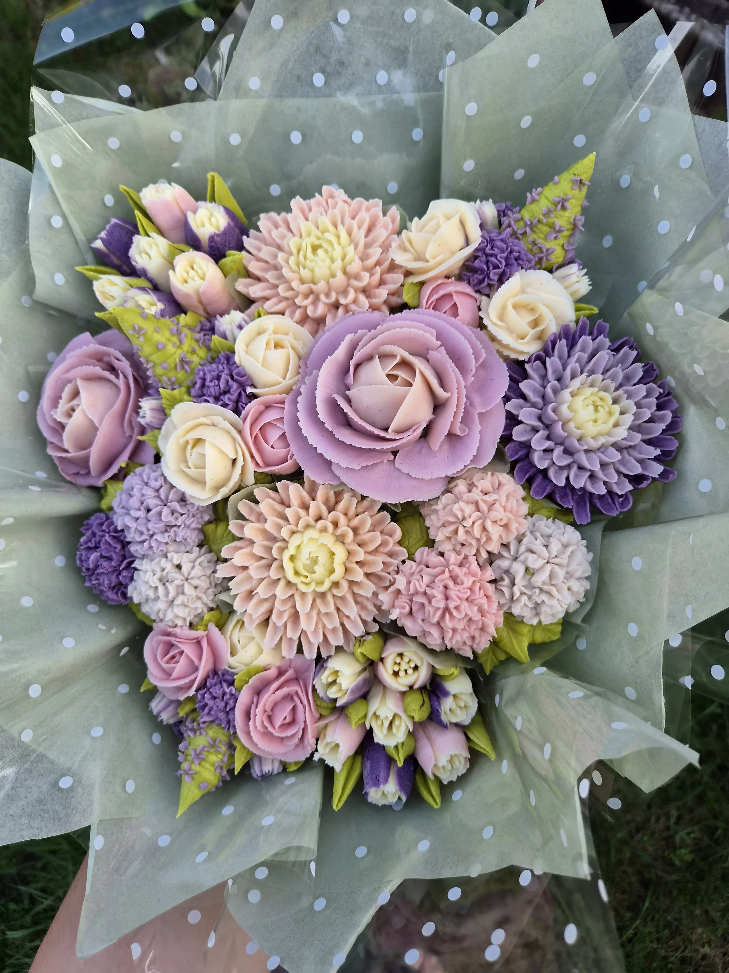 Close-up of a vanilla bean cupcake bouquet of various pastel-colored artificial flowers wrapped in transparent polka-dot paper.