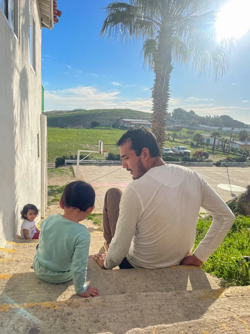 A Mexican child sitting on concrete steps outside next to a Mexican man at St. Innocent Orphanage