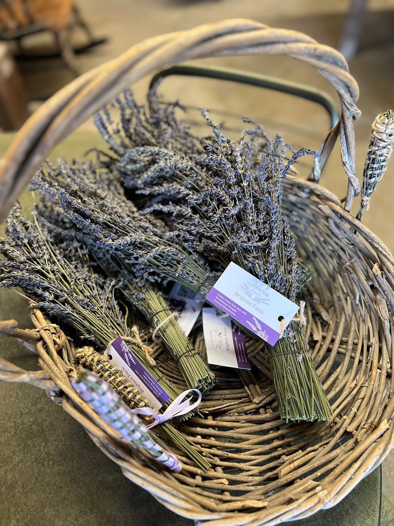 A woven basket filled with bundles of dried lavender flowers, each bundle wrapped with a purple and white label, sitting on a dark surface.