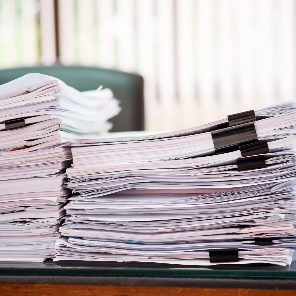 Tall stack of paper files and documents on a desk