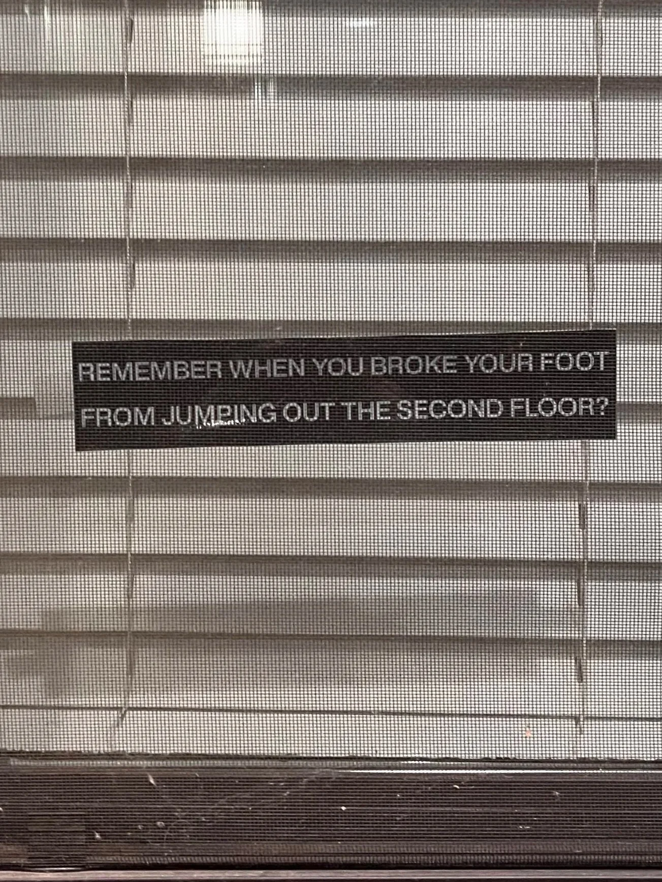 A sign on a window screen that reads: 'Remember when you broke your foot from jumping out the second floor?'