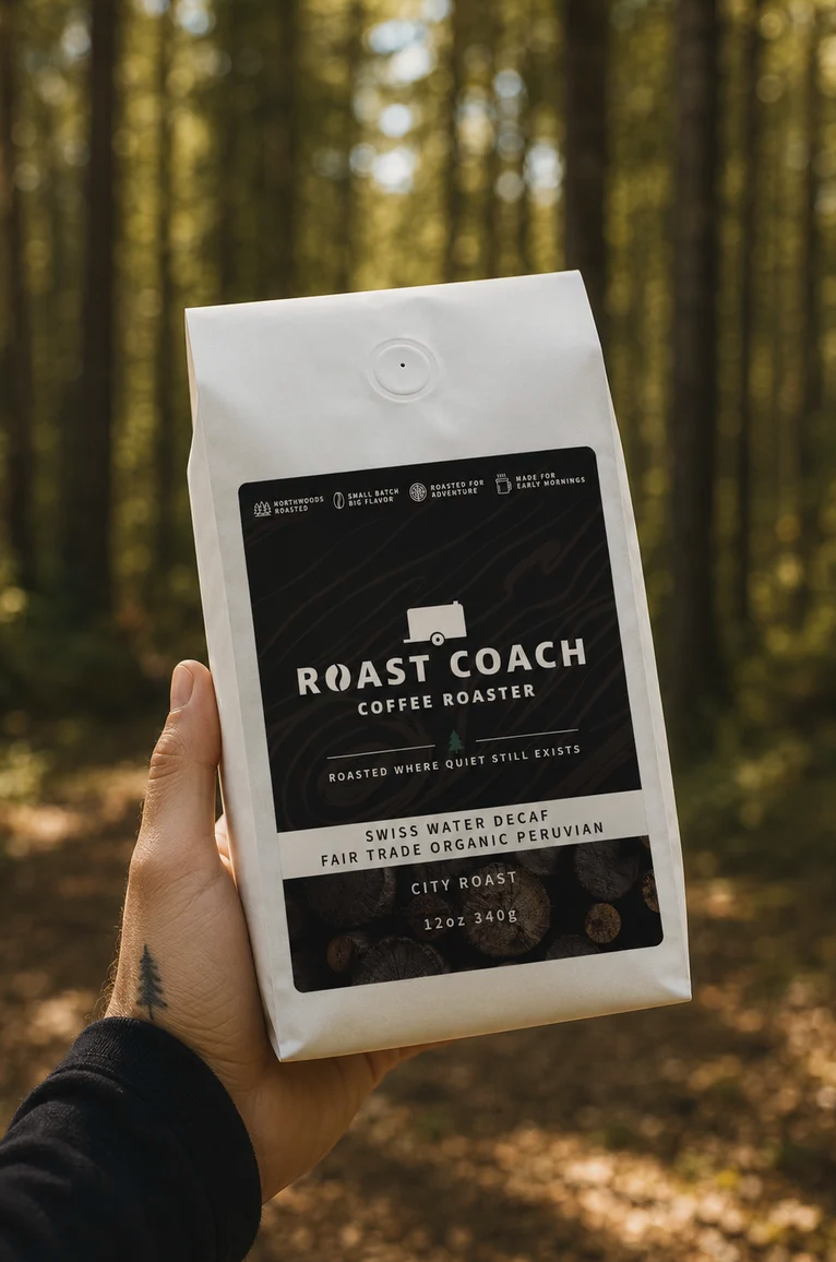 Hand holding a bag of roast coffee beans outdoors in a forest with sunlight filtering through trees.