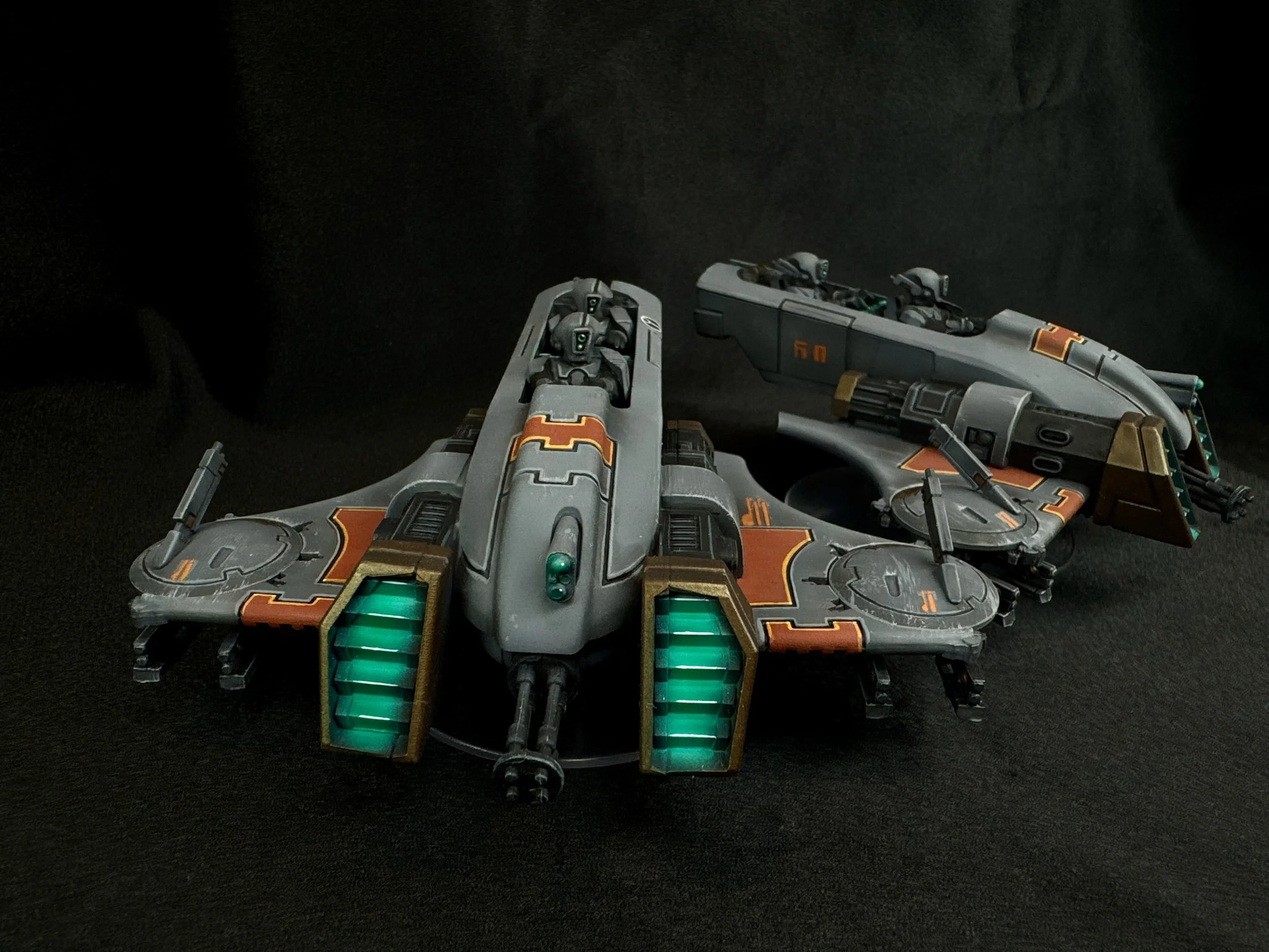 A futuristic toy spaceship with gray, black, and orange details, and glowing green engine parts, positioned on a black surface.
