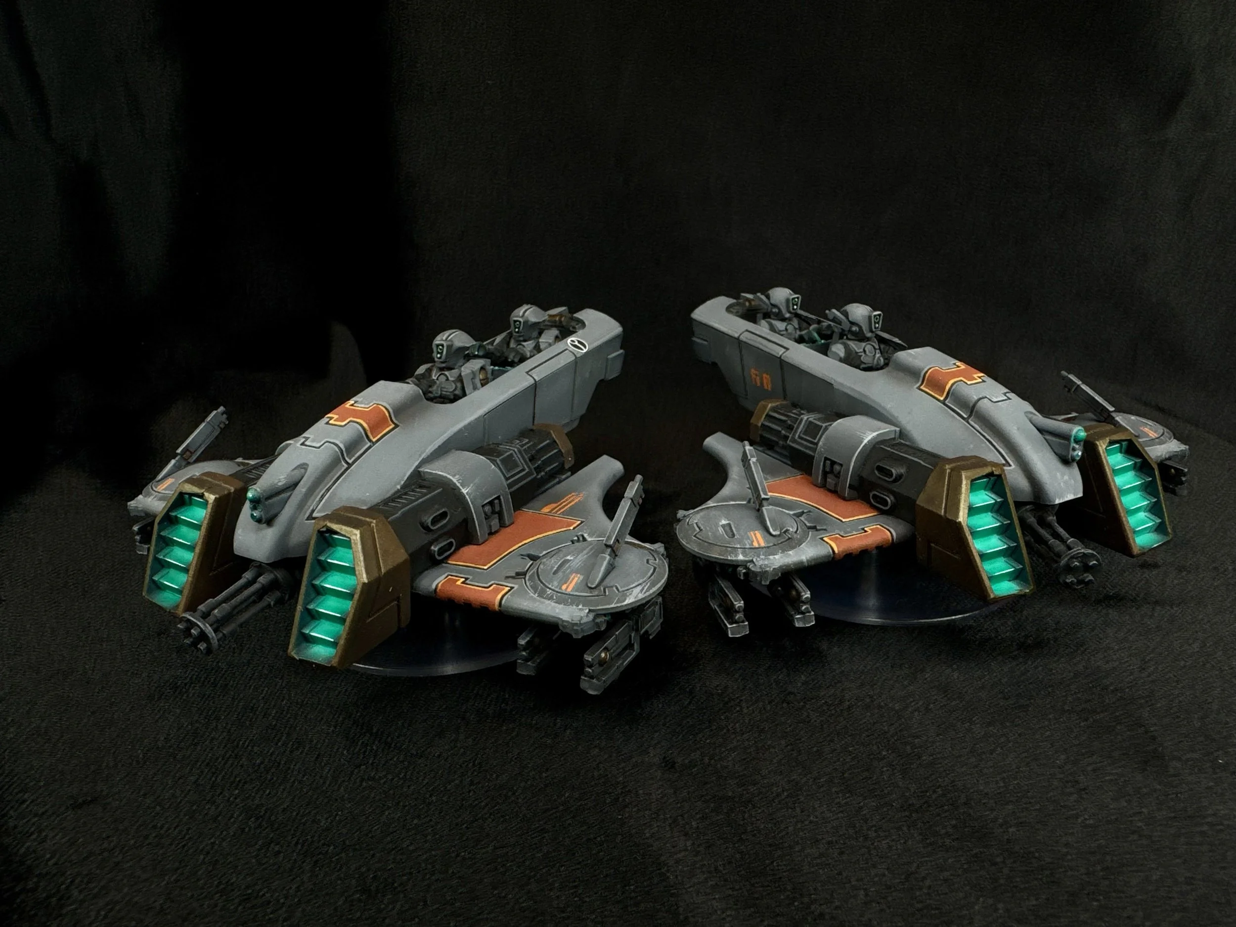 Two futuristic robotic vehicles with sleek, aerodynamic design, glowing green lights, and orange decorative markings are displayed against a plain black background.
