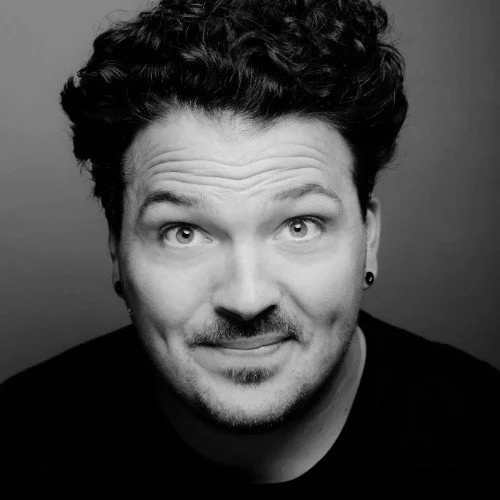 Black and white portrait of a man with curly hair, smiling slightly, looking directly at the camera.