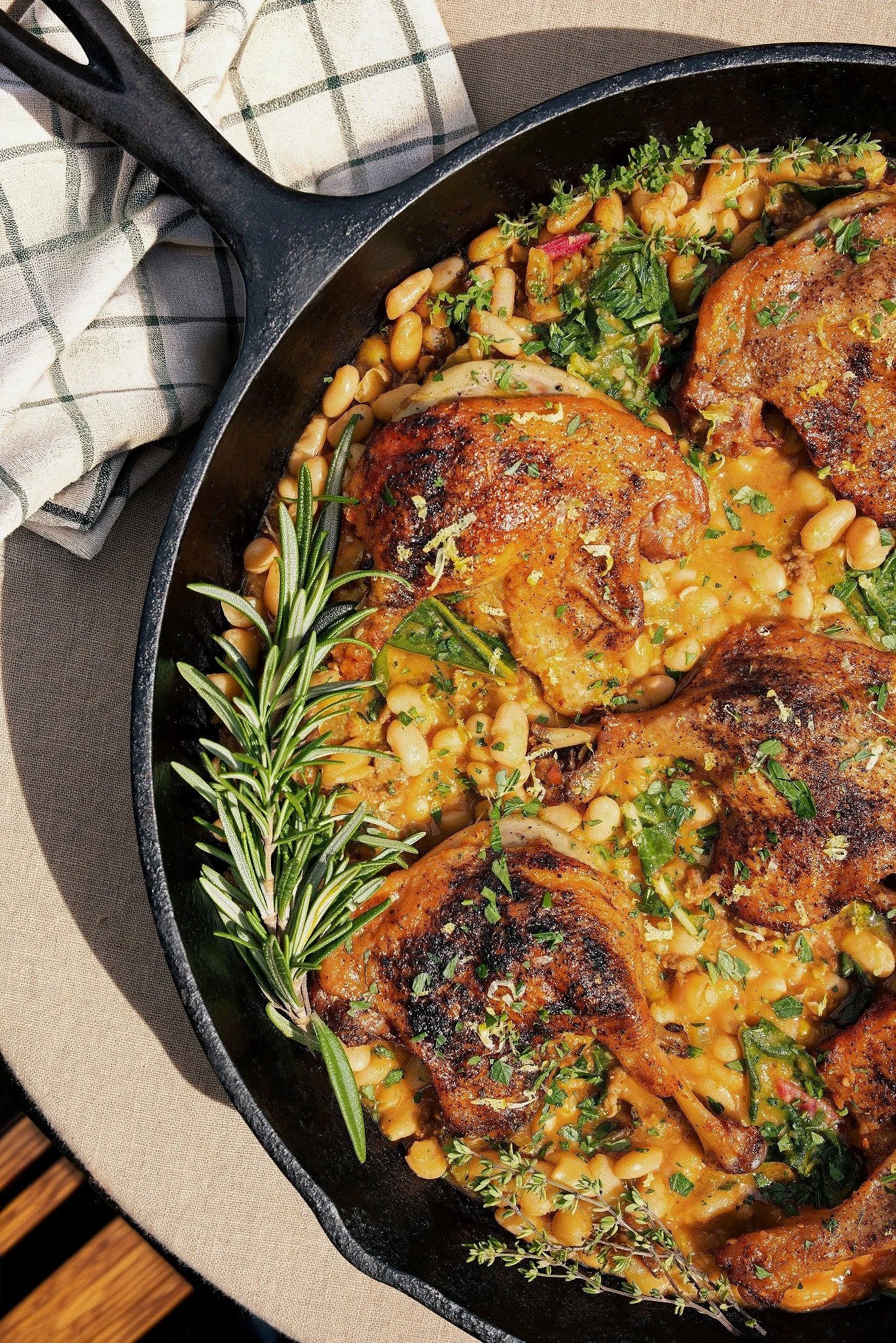 Hospitality — Rustic cassoulet with browned chicken, white beans, greens, and fresh herbs photographed for an editorial recipe story.