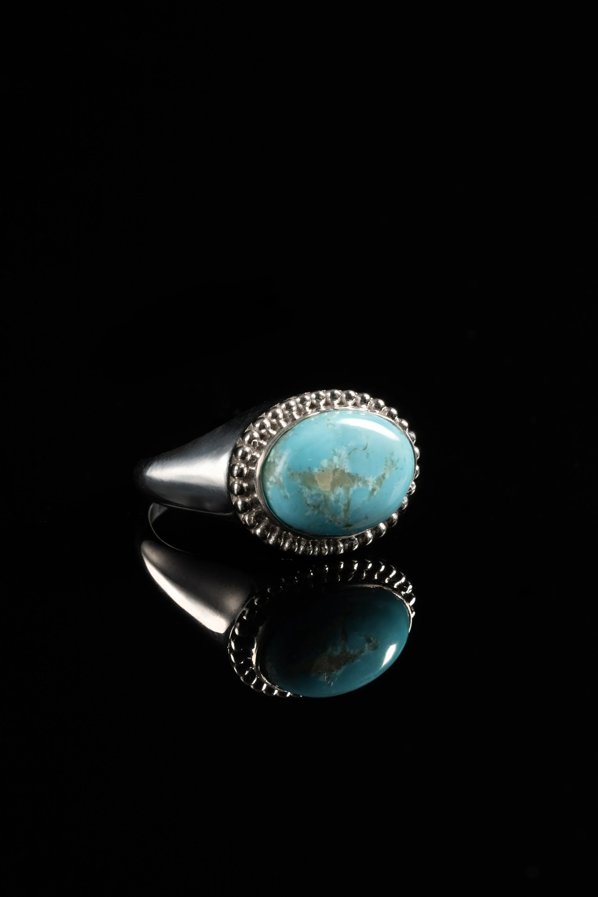 Luxury Jewelry — Turquoise gemstone ring photographed on black with a reflective product composition.