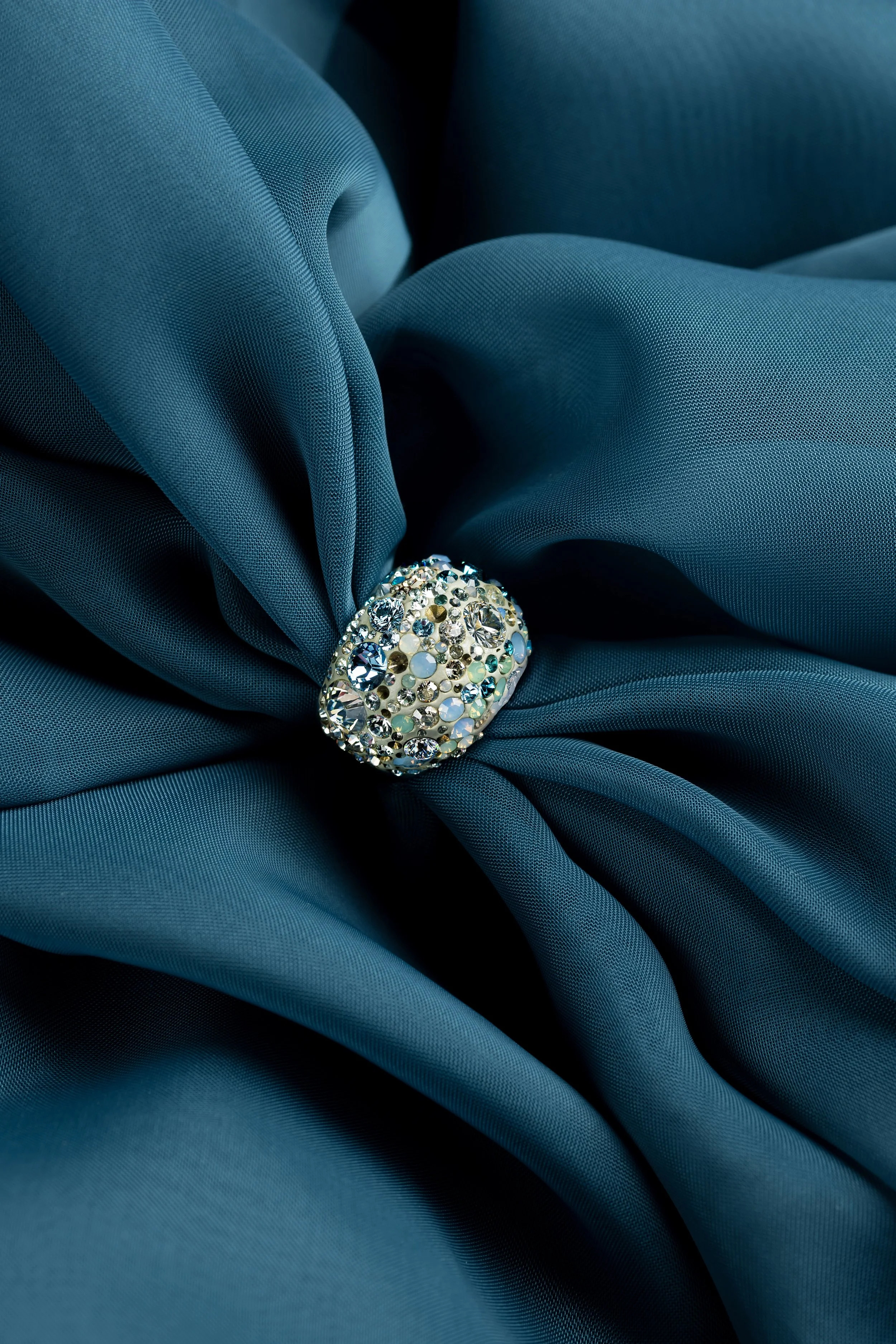 Editorial & Brand — Swarovski ring styled against sculptural blue fabric for a luxury jewelry editorial.