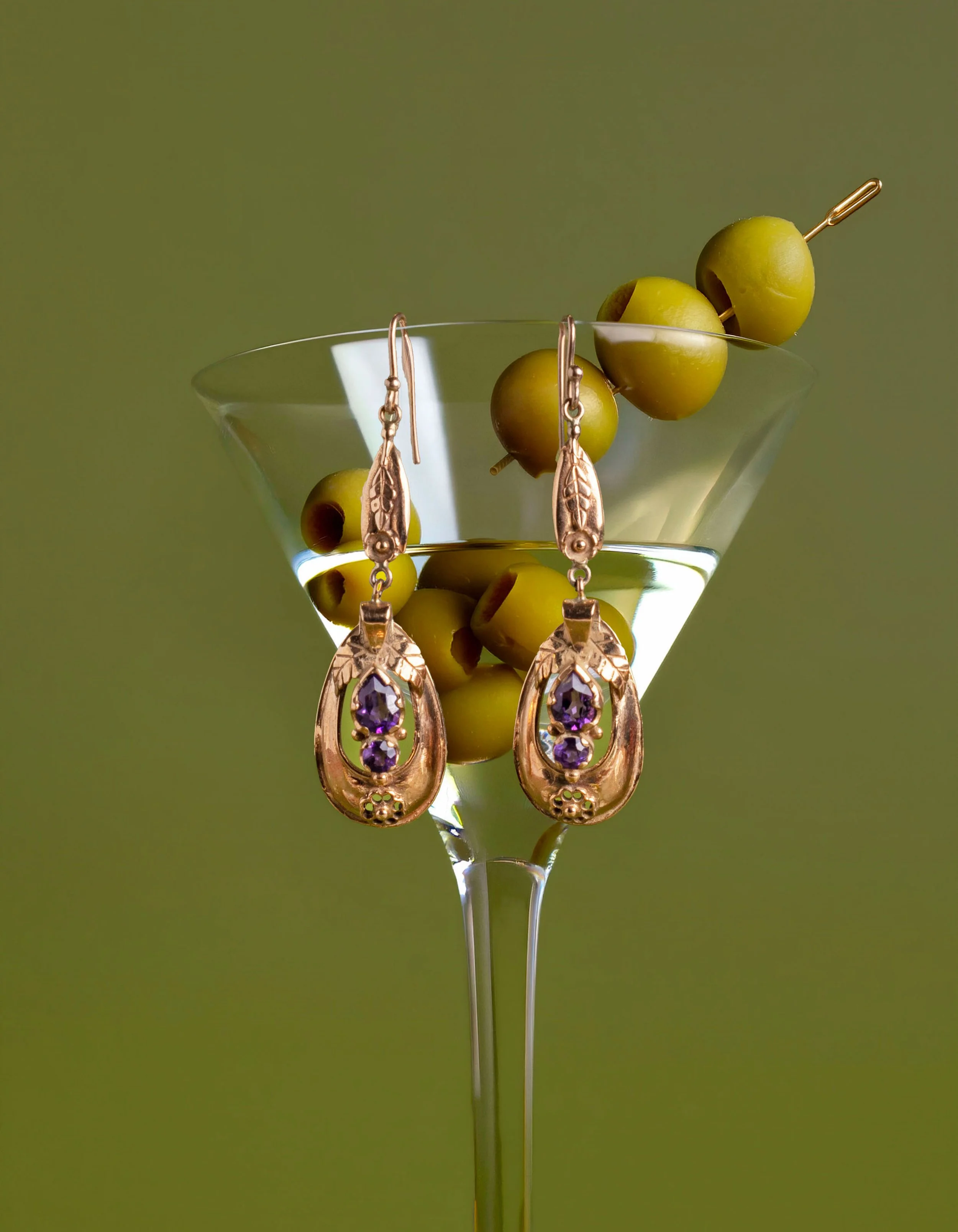 Luxury gemstone earrings styled over a martini glass with green olives, editorial jewelry photography by Fraiche Photography.