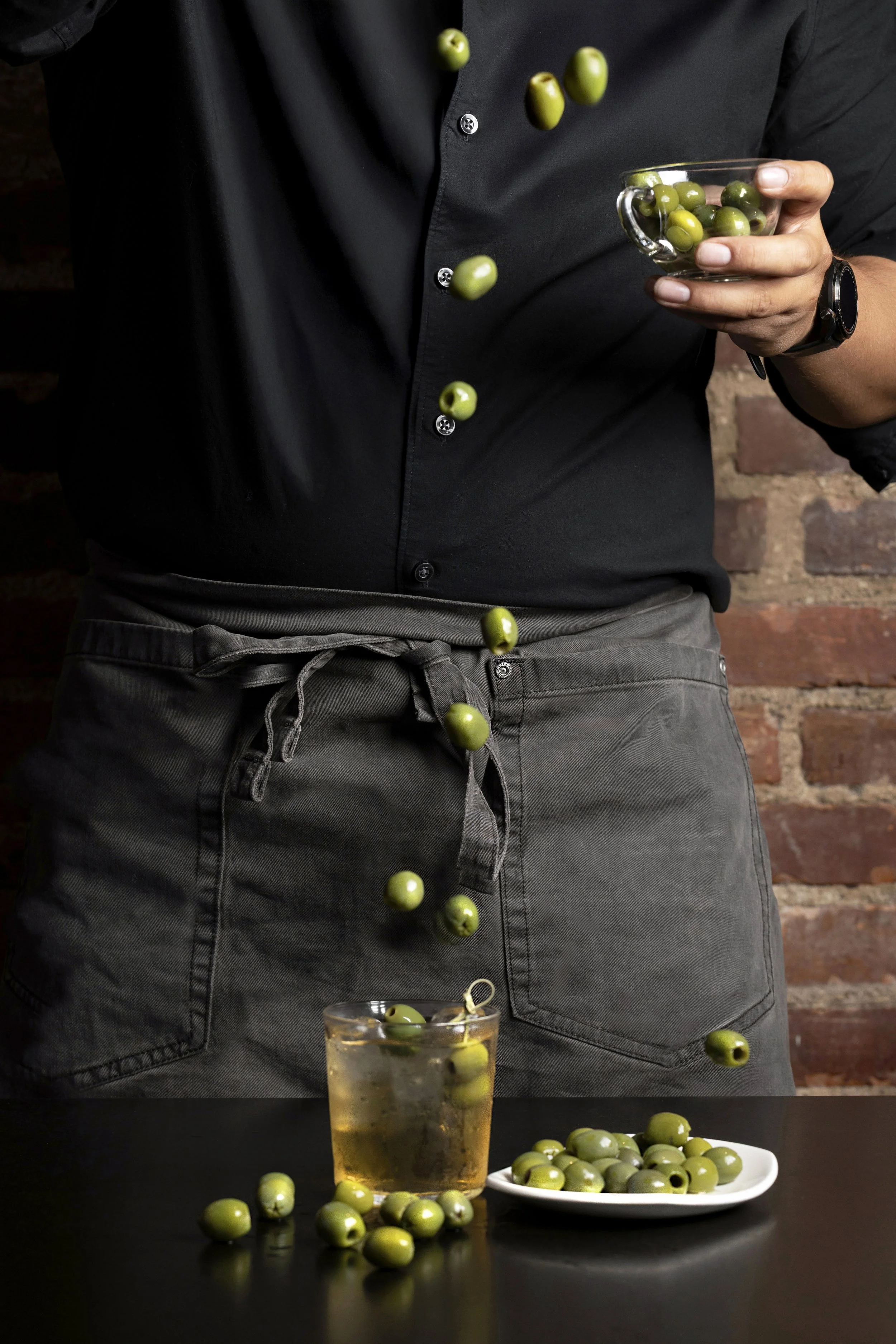 Sherry tonic cocktail with olives in a dark editorial setting, photographed for a food and beverage campaign.