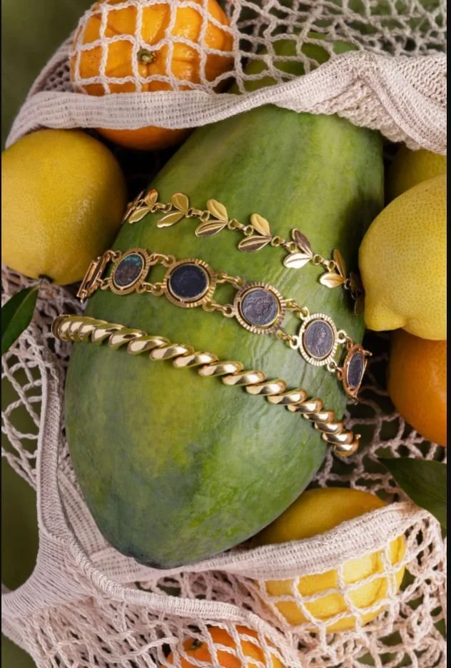 Luxury Jewelry — Gold bracelets and gemstone rings styled with papaya and citrus for a warm editorial still life.