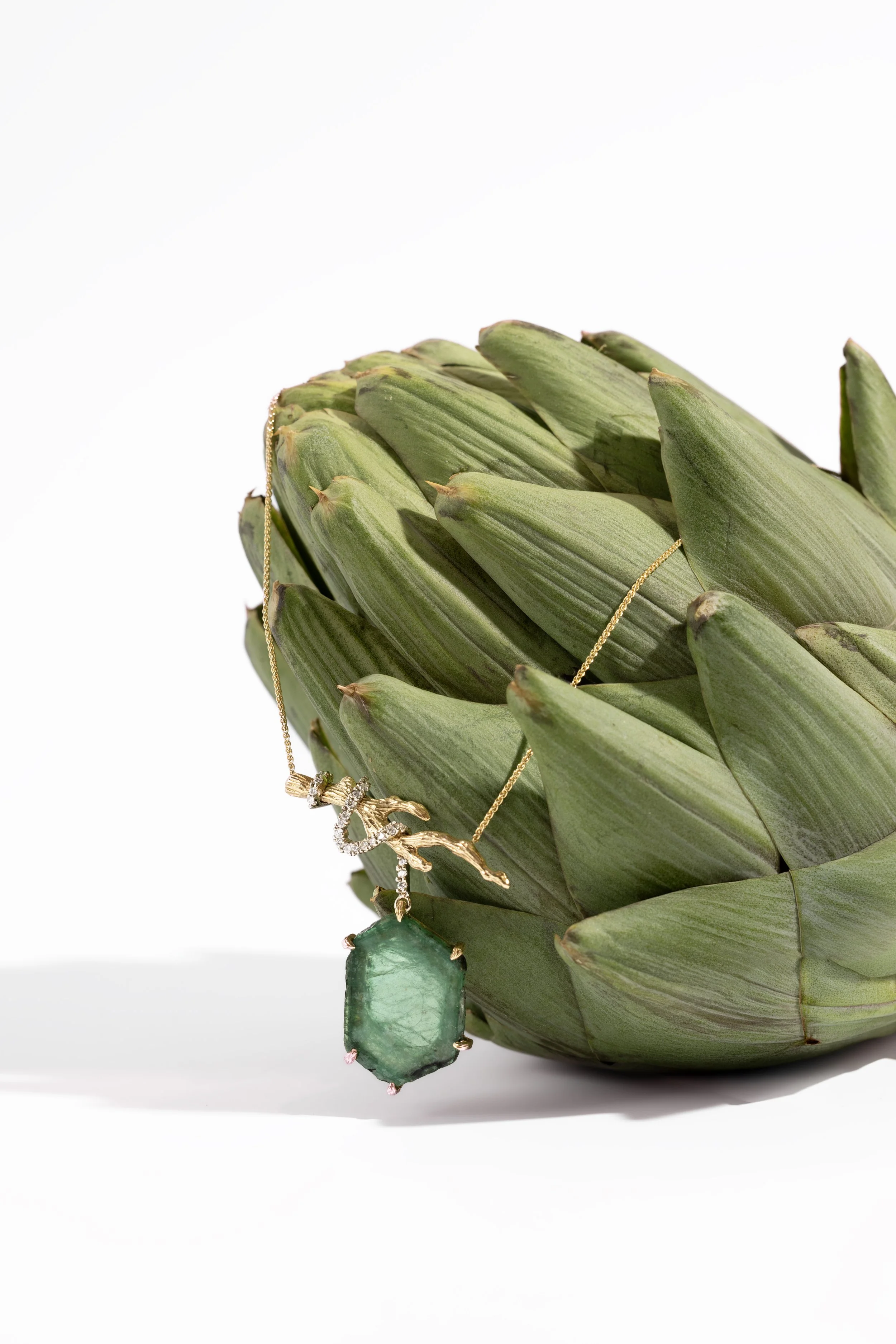 Luxury Jewelry — Emerald pendant necklace styled with artichoke leaves for an organic editorial still life.
